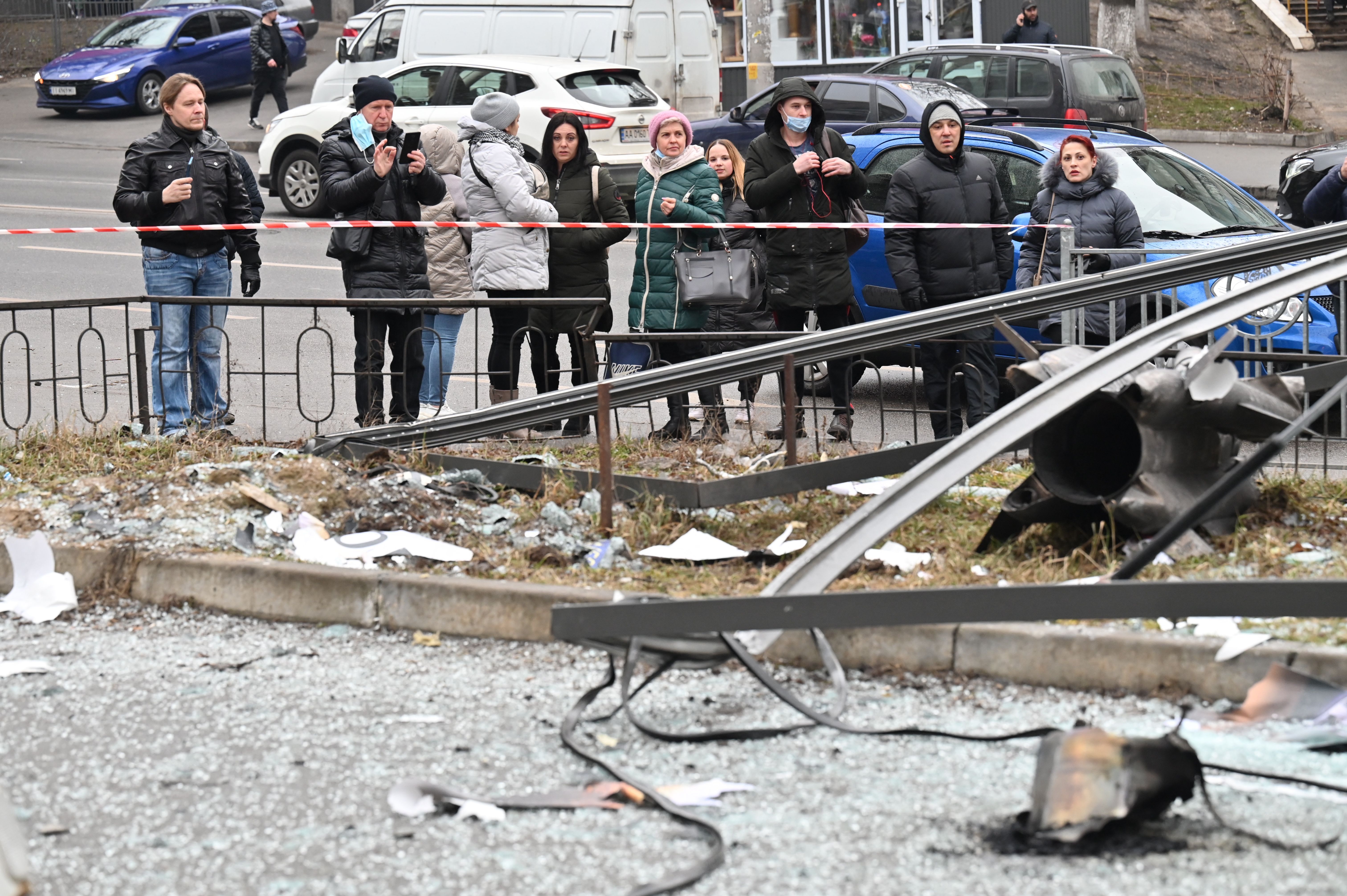 People react standing behind the cordoned off area around the remains of a shell in Kyiv on February 24