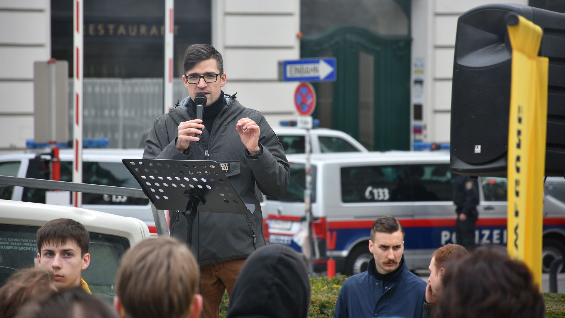 In this image, Martin Sellner stands and speaks into a microphone.