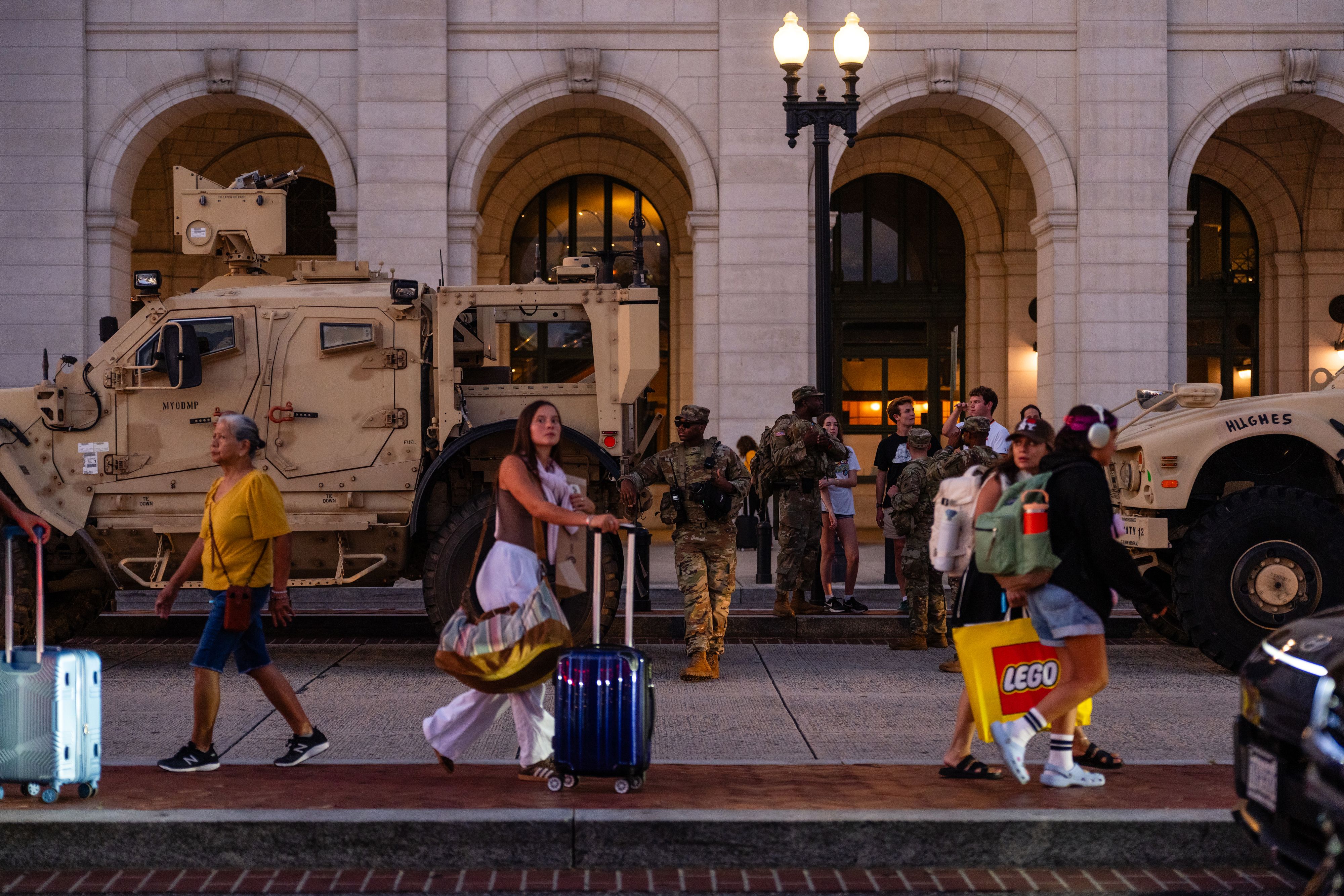Travelers toting luggage walk past National Guard troops at Union Station in Washington on Thursday evening, Aug. 14, 2025. As President Donald Trump's federal takeover of law enforcement in the nation's capital ramps up, the National Guard will build up on Thursday and Friday to send out about 100