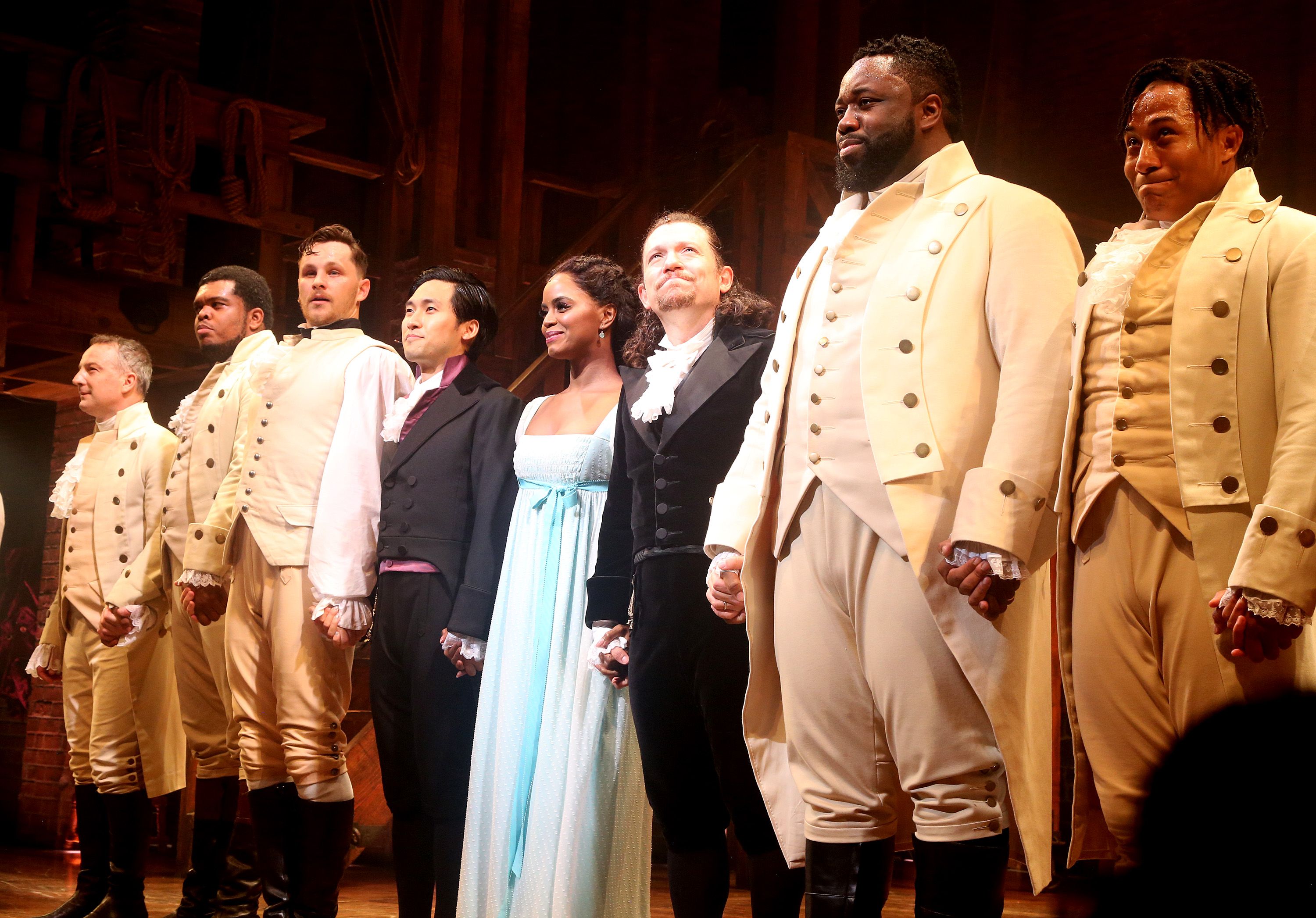 Picture of the "Hamilton" cast holding hands and looking out at the crowd