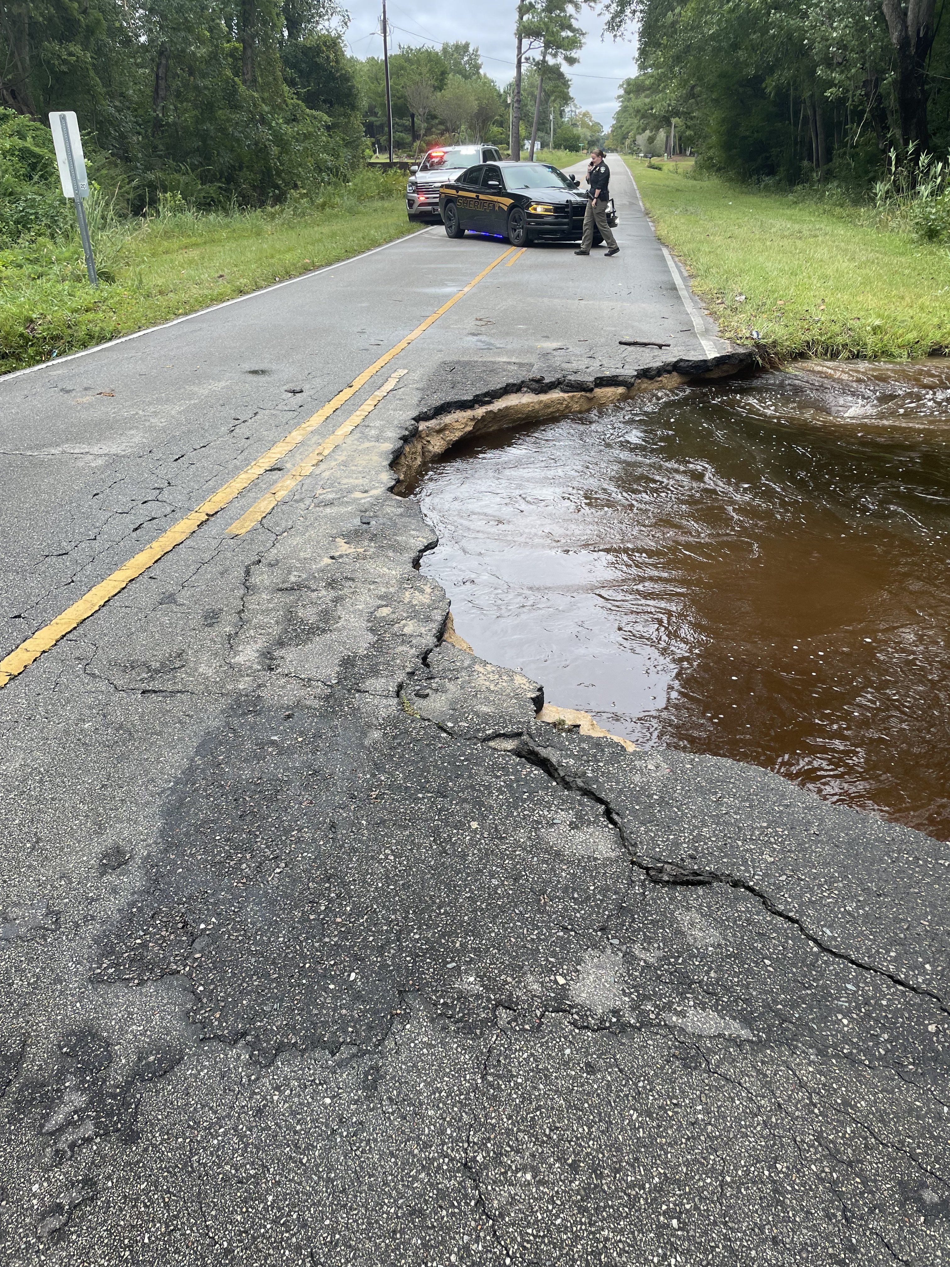 A hole in a Brunswick County, N.C. road is filled with water as police block the road with their car nearby. An officer can be seen outside the vehicle.