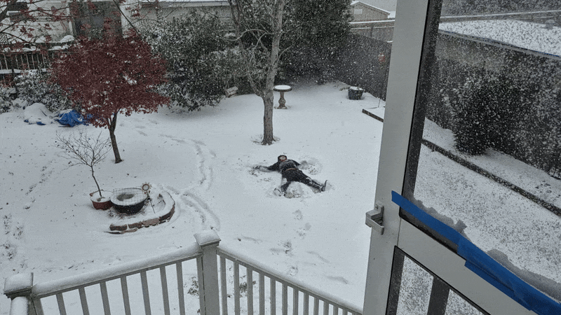 A boy makes a snow angel, viewed from a patio above him.