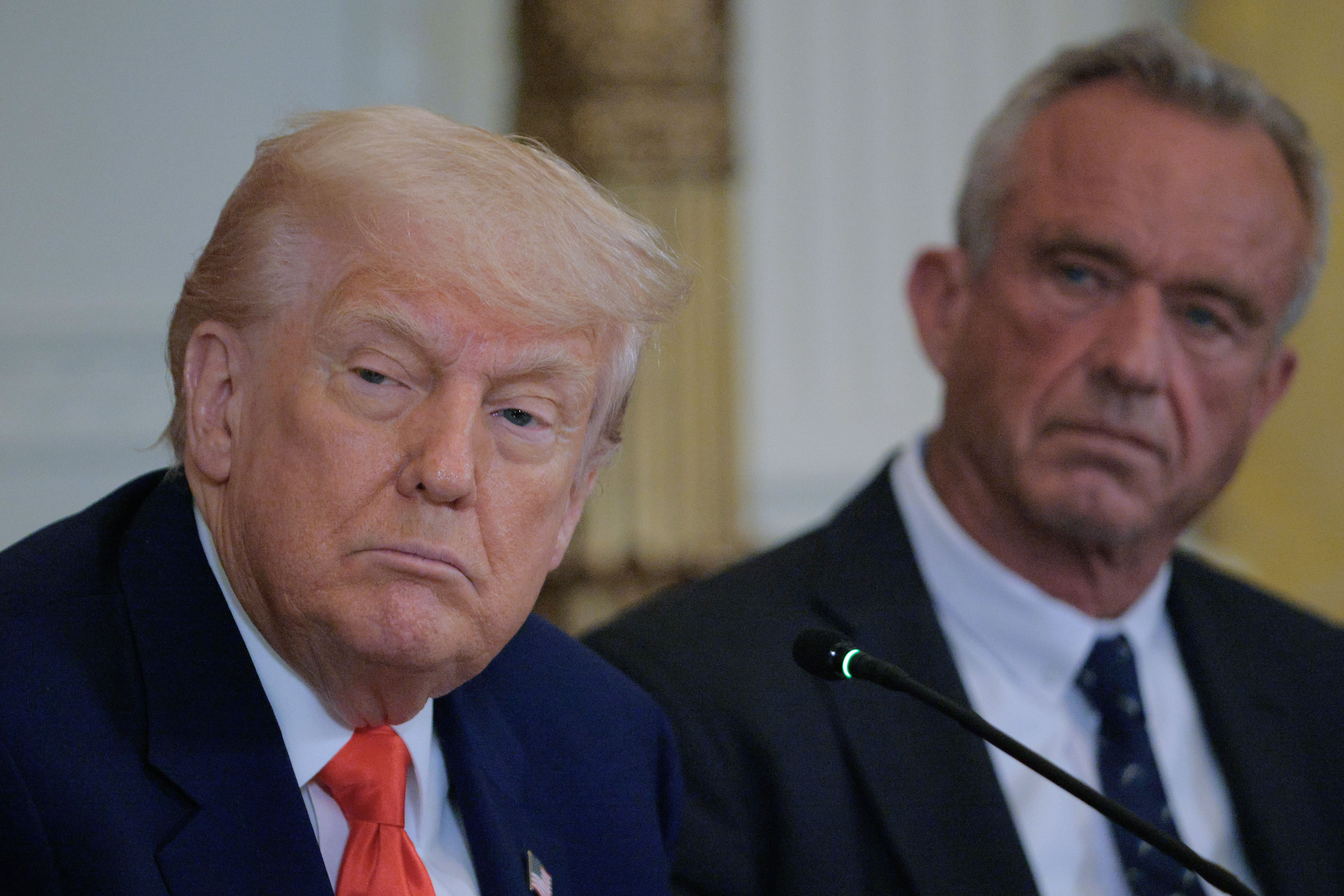 President Donald Trump stands beside HHS Secretary Robert F. Kennedy Jr. in the East Room of the White House.