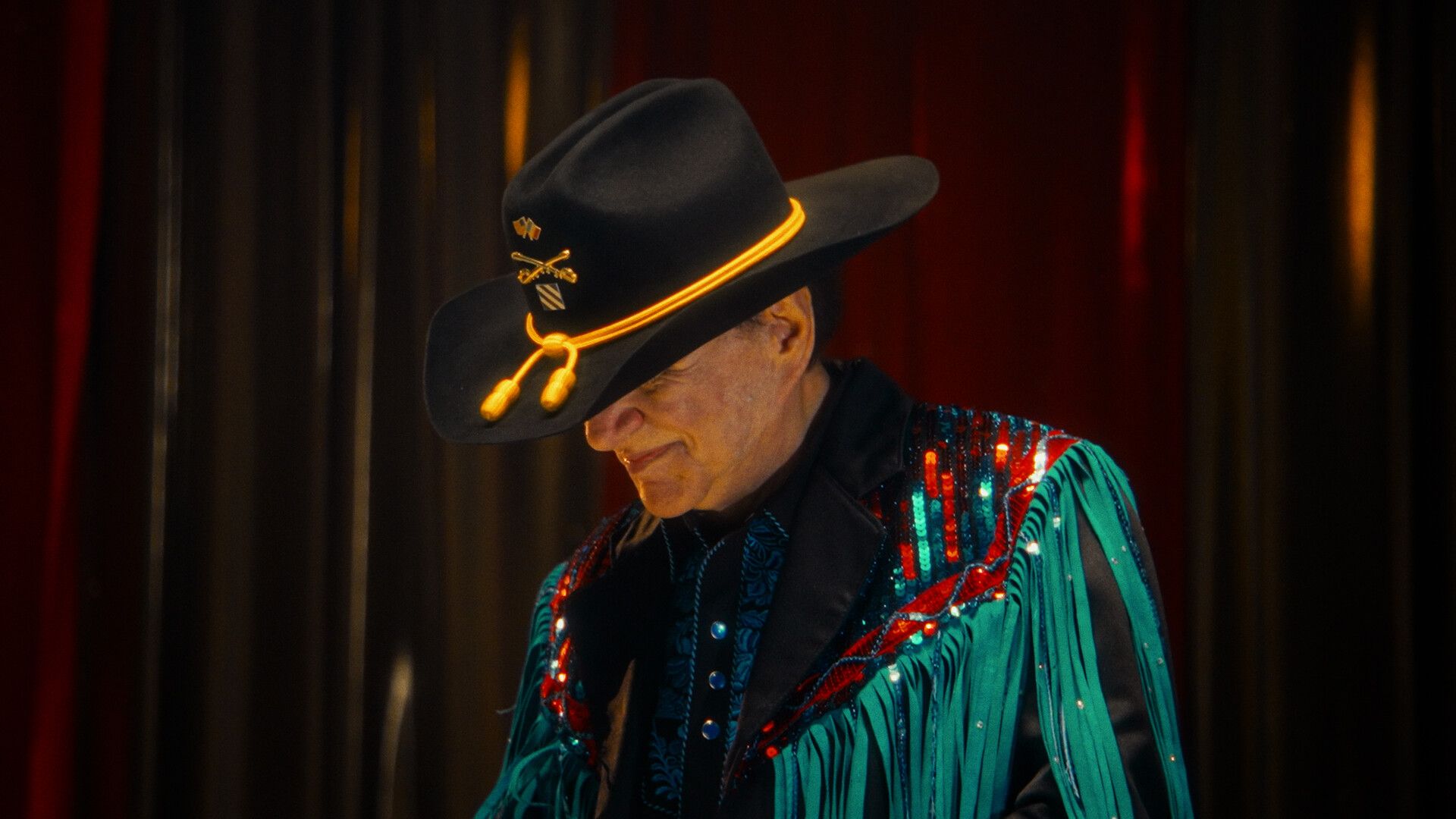 A movie still of Johnny Canales in a hat looking down.