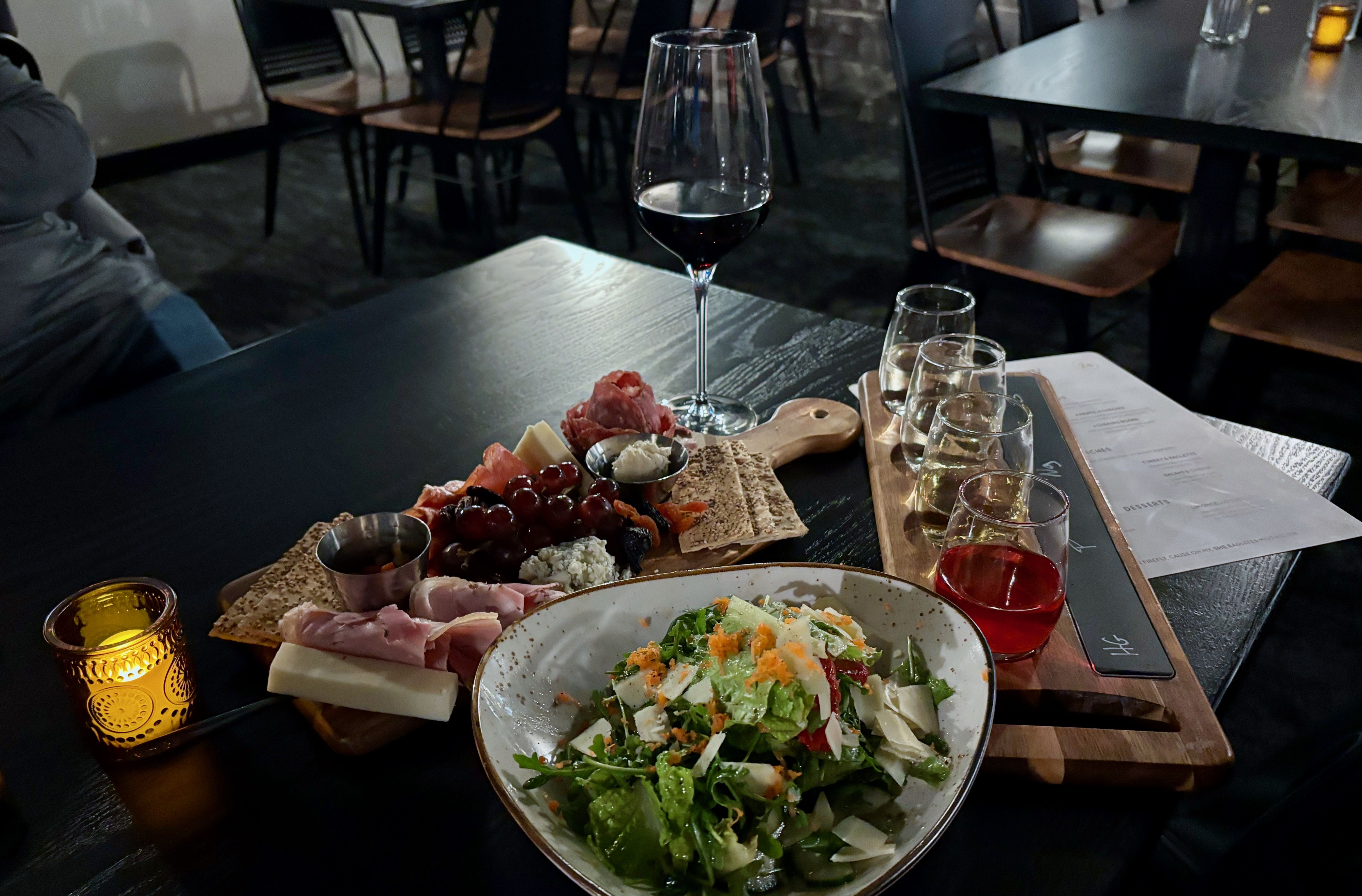 A photo of the food Alissa ate and wine flight she drank — a charcuterie board, a salad, four small wine glasses and a tall glass of wine