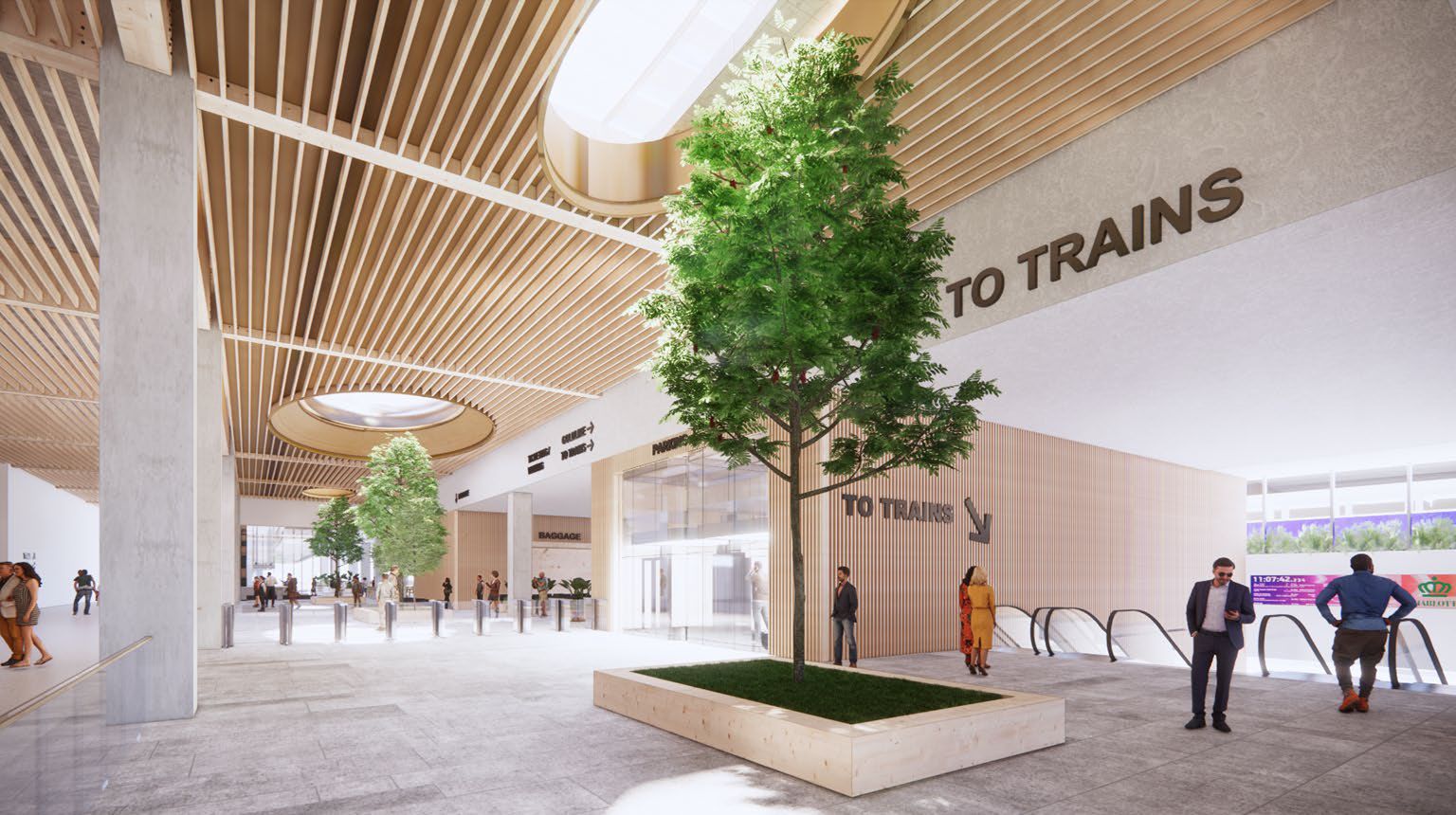 Spacious, modern train station interior with wooden slat ceiling, indoor trees in planter boxes, escalators, signage pointing "TO TRAINS," and people walking or standing around.