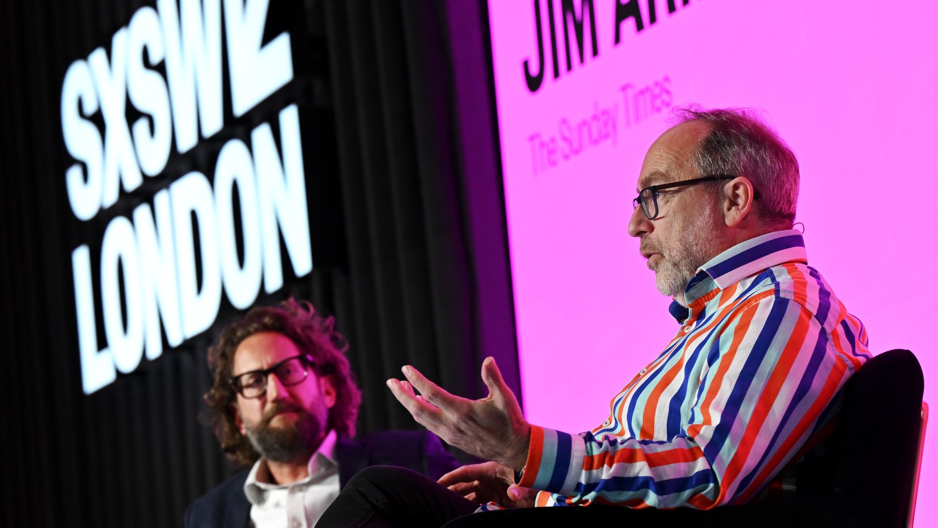Jimmy Wales, Wikipedia founder, speaks on stage with Jim Armitage, and a lit banner in the back reading, "SXSW London."
