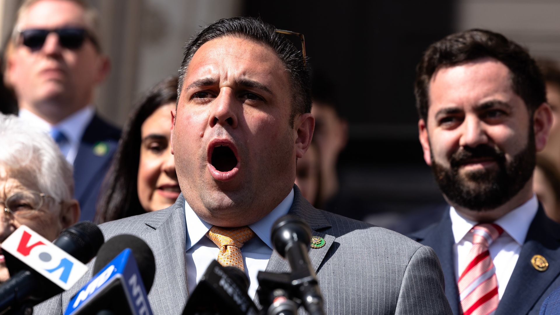 Rep. Anthony D'Esposito, wearing a gray suit and speaking into microphones while flanked by colleagues.