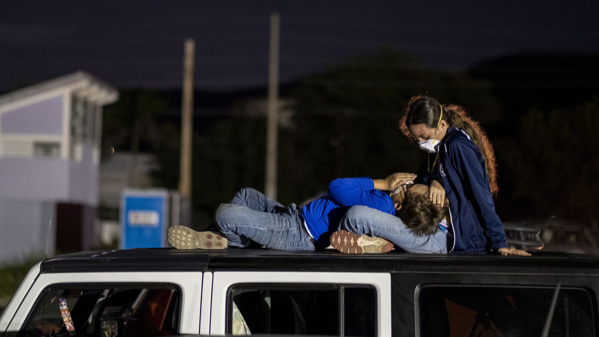 In this image, a child rests their head in a woman's lap on top of a car in Puerto Rico.