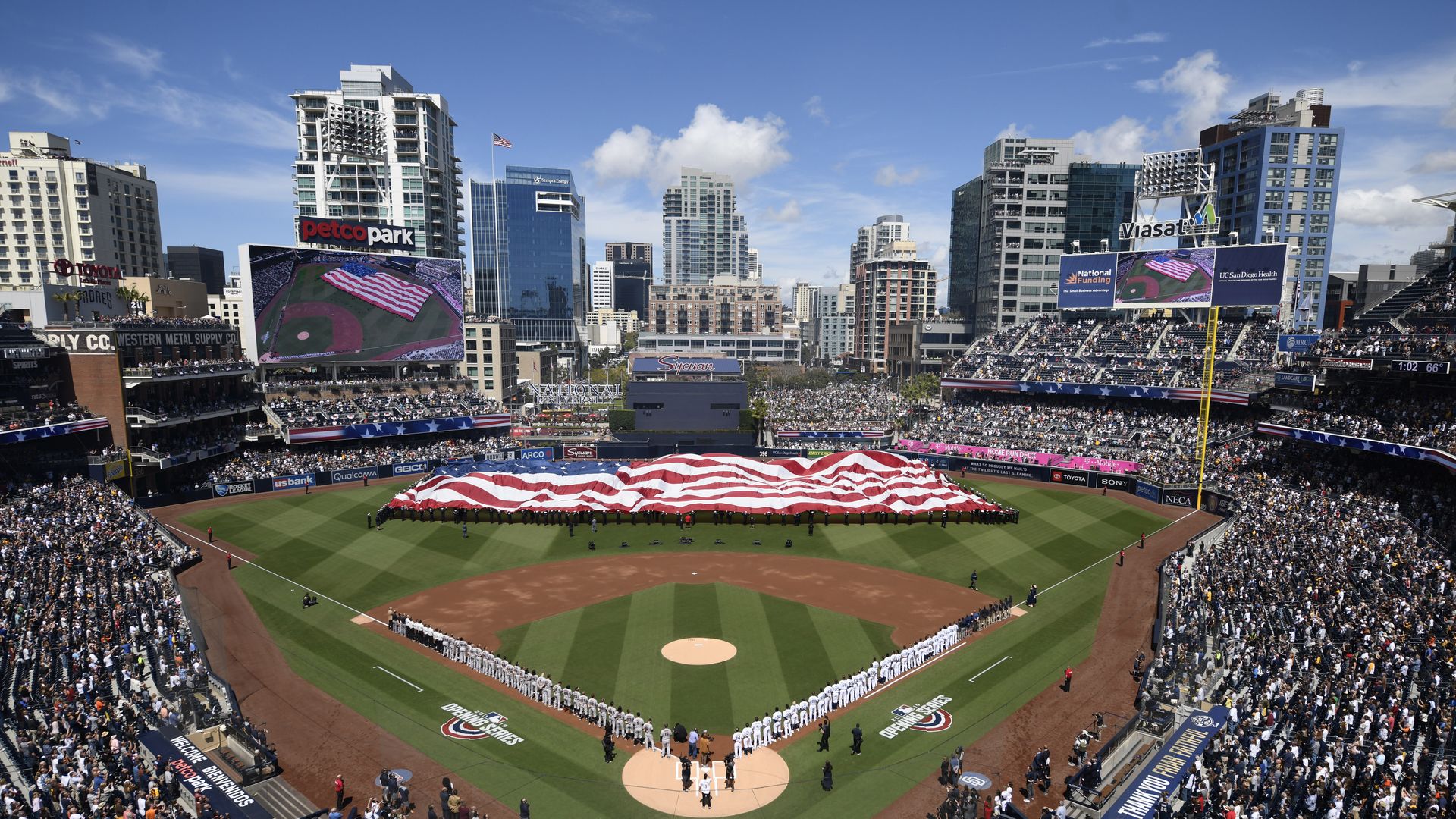 Petco Park with a large American flag in the outfield and the city skyline beyond the park