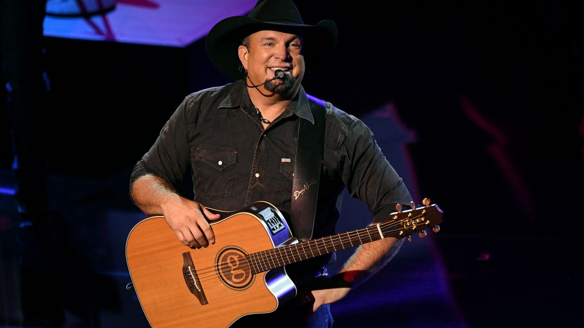 Garth Brooks holding a guitar and laughing with the audience.