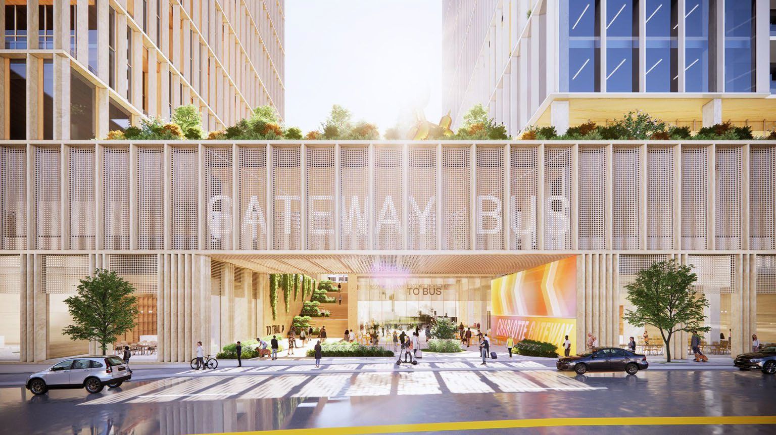 Sunlit, modern Gateway Building entrance with large glass doors, people walking and biking, greenery and cars parked on a reflective street in an urban setting.