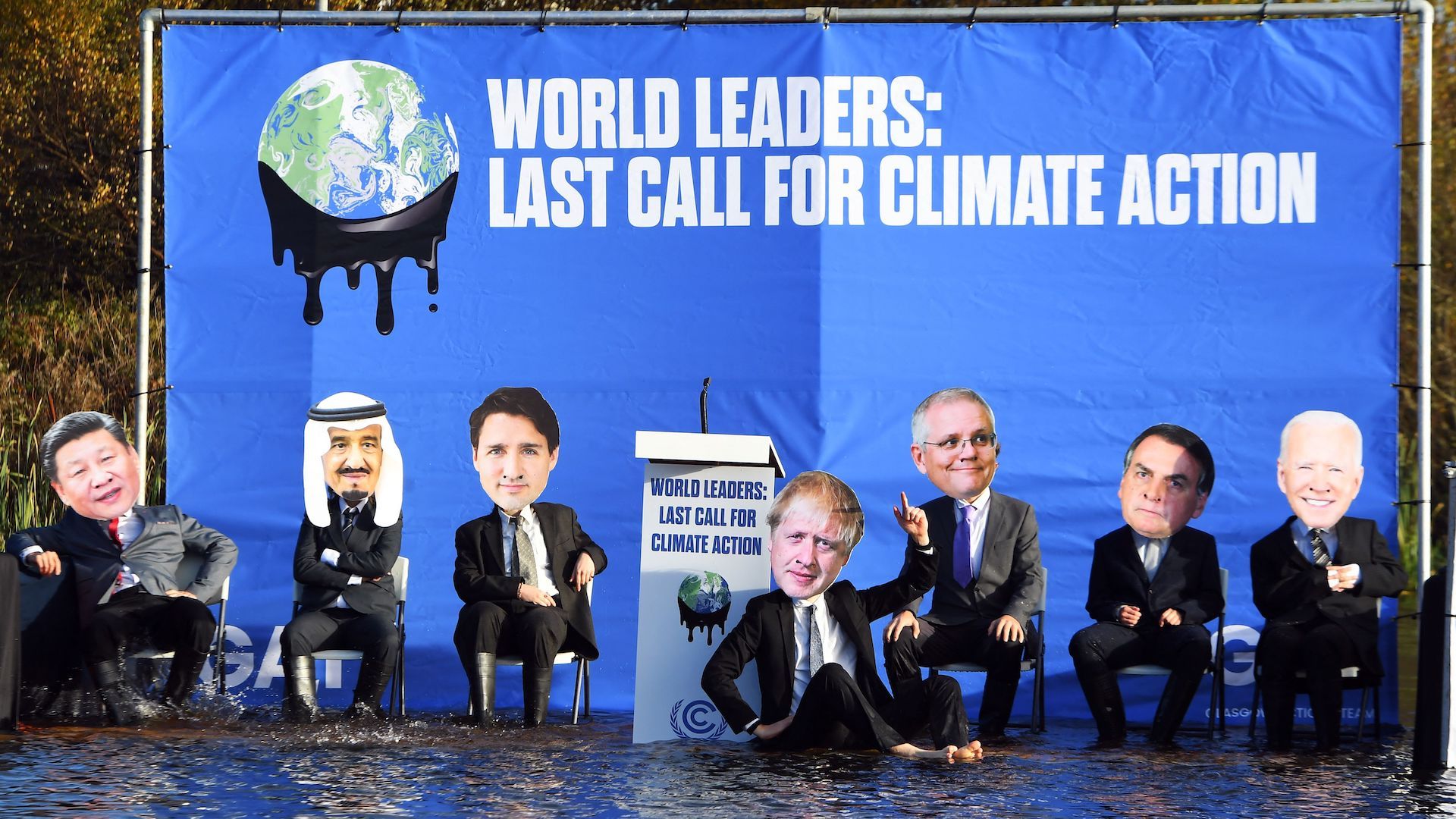 Protest at COP26 showing world leaders sinking into a river with "Last Call for Climate Action" sign.