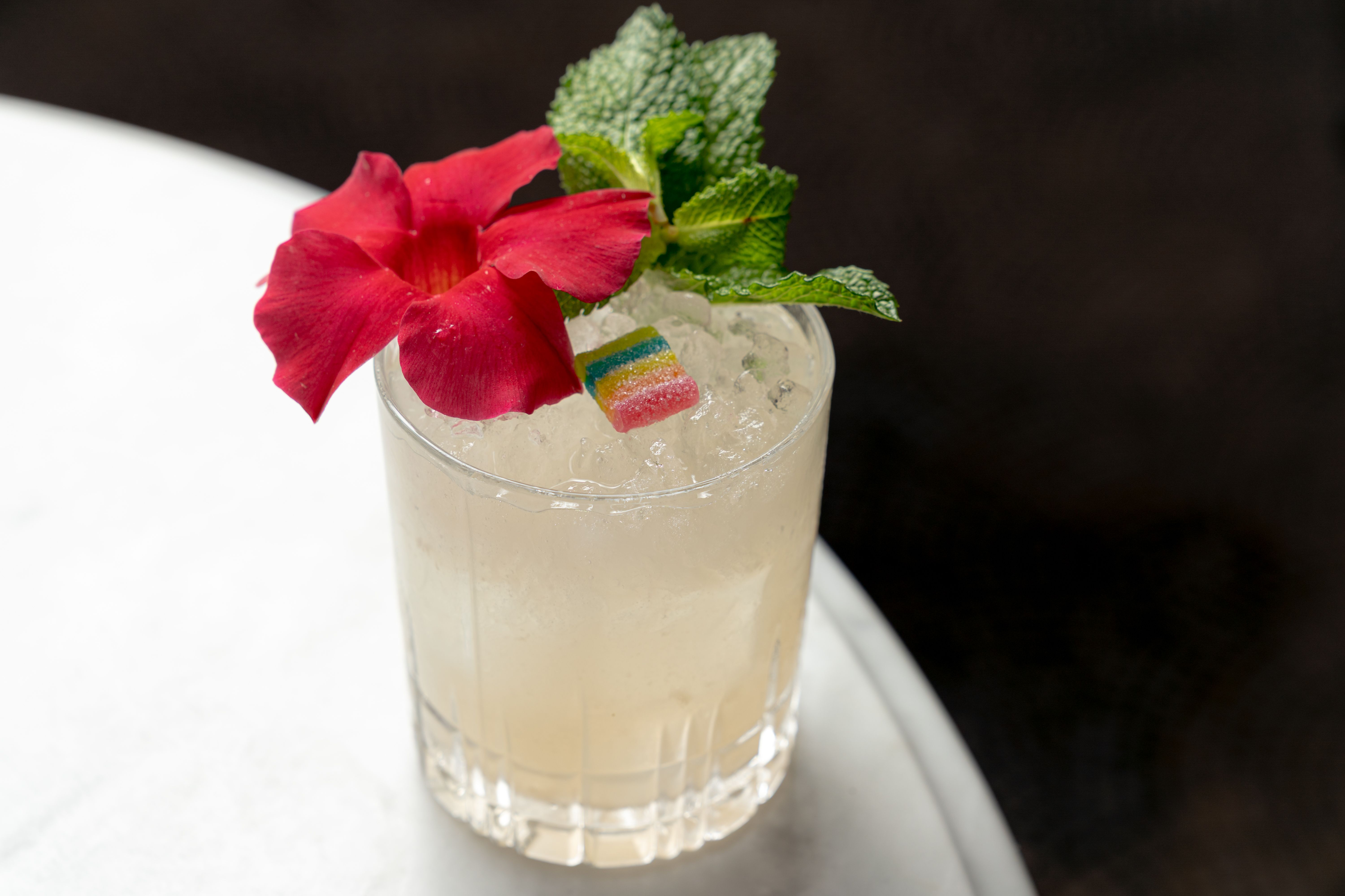 A cocktail with a red flower, mint and a multi-colored candy.