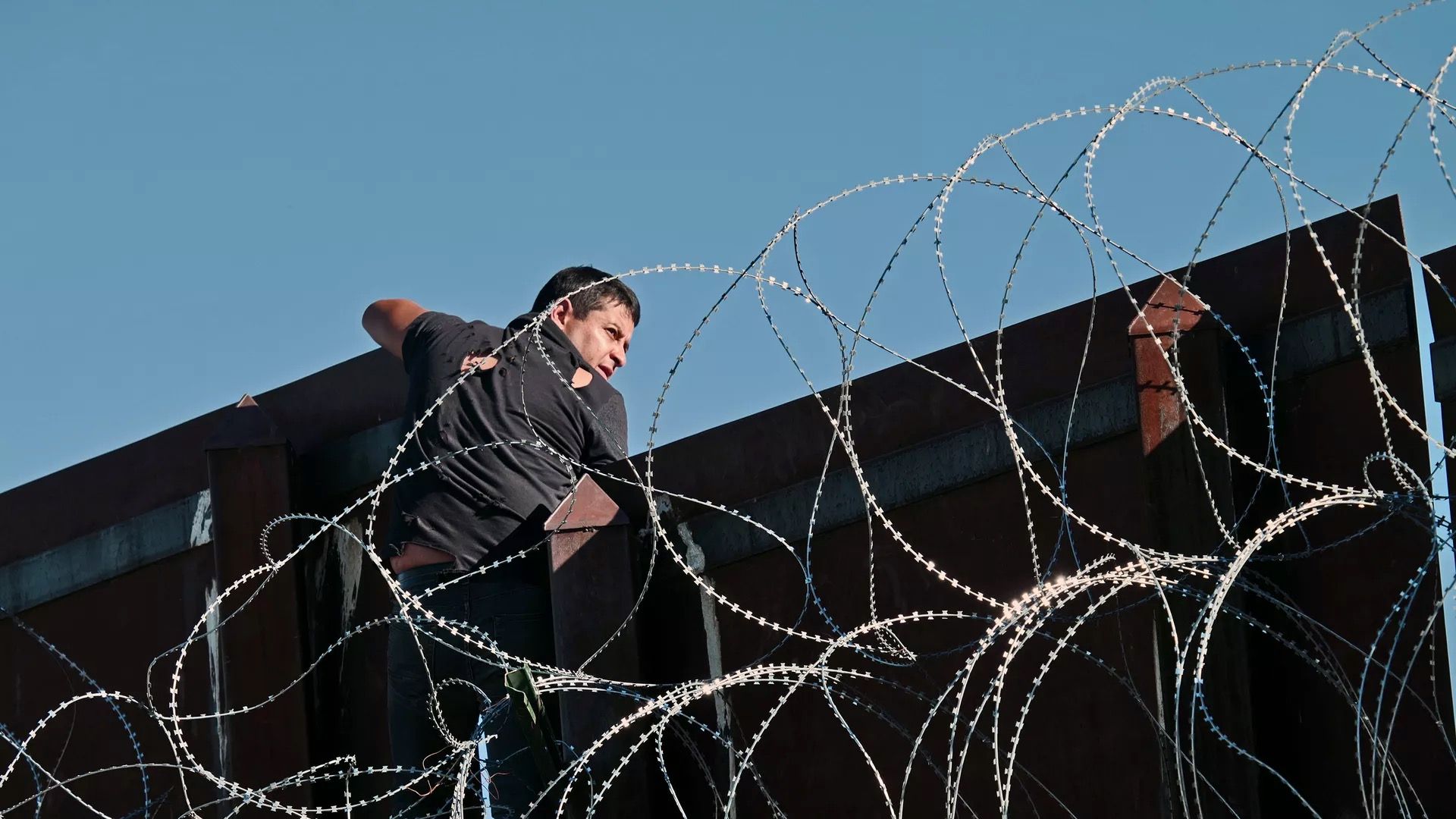 A man is seen scaling the U.S.-Mexico border wall.
