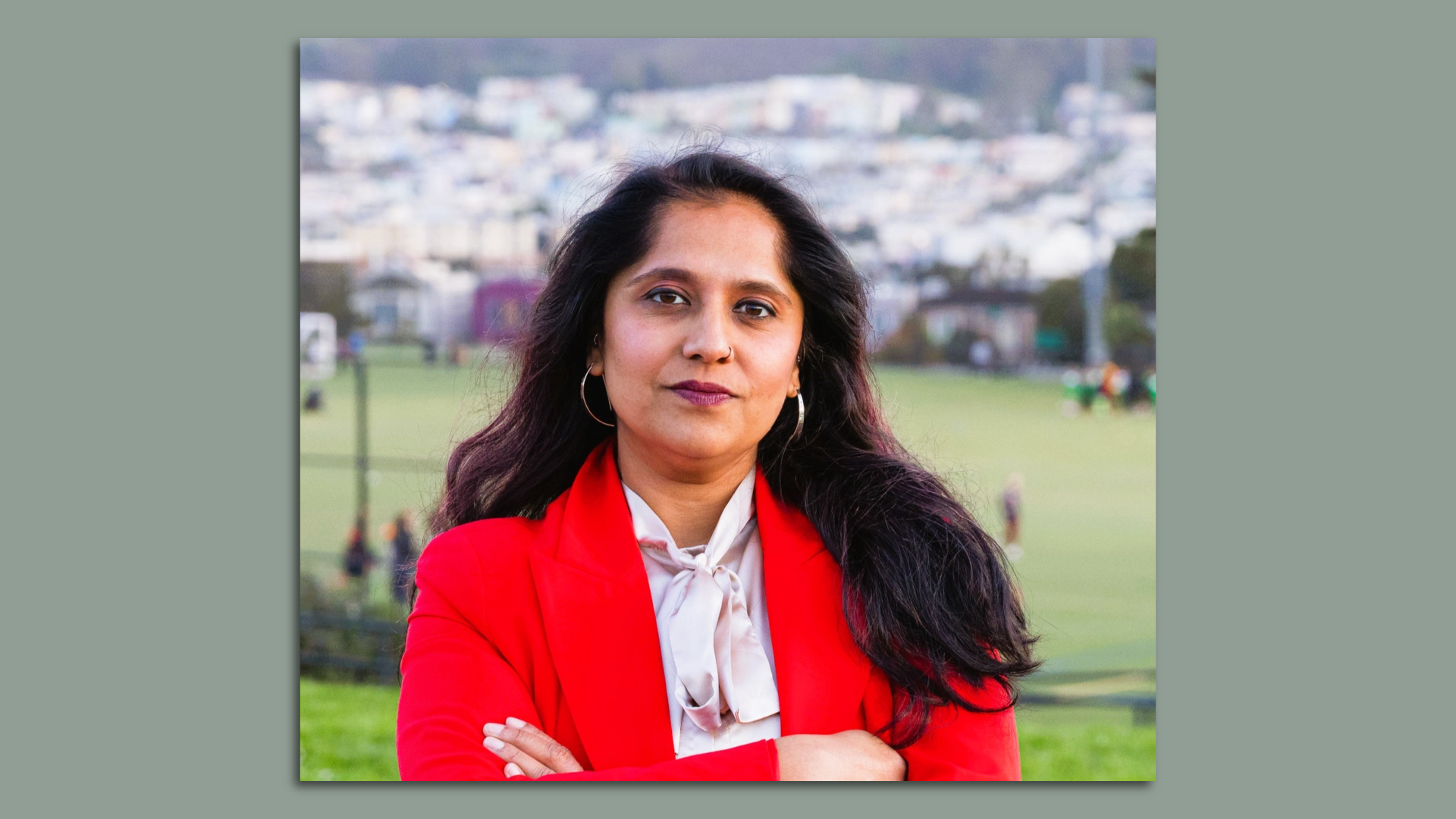 Photo of Adlah Chisti in a red blazer and white top looking at the camera while crossing her arms
