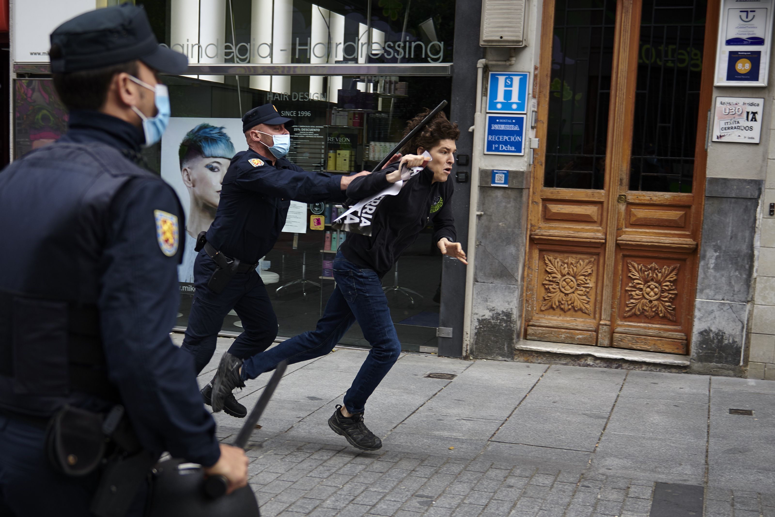 In this image, a man runs from police that are wearing face masks