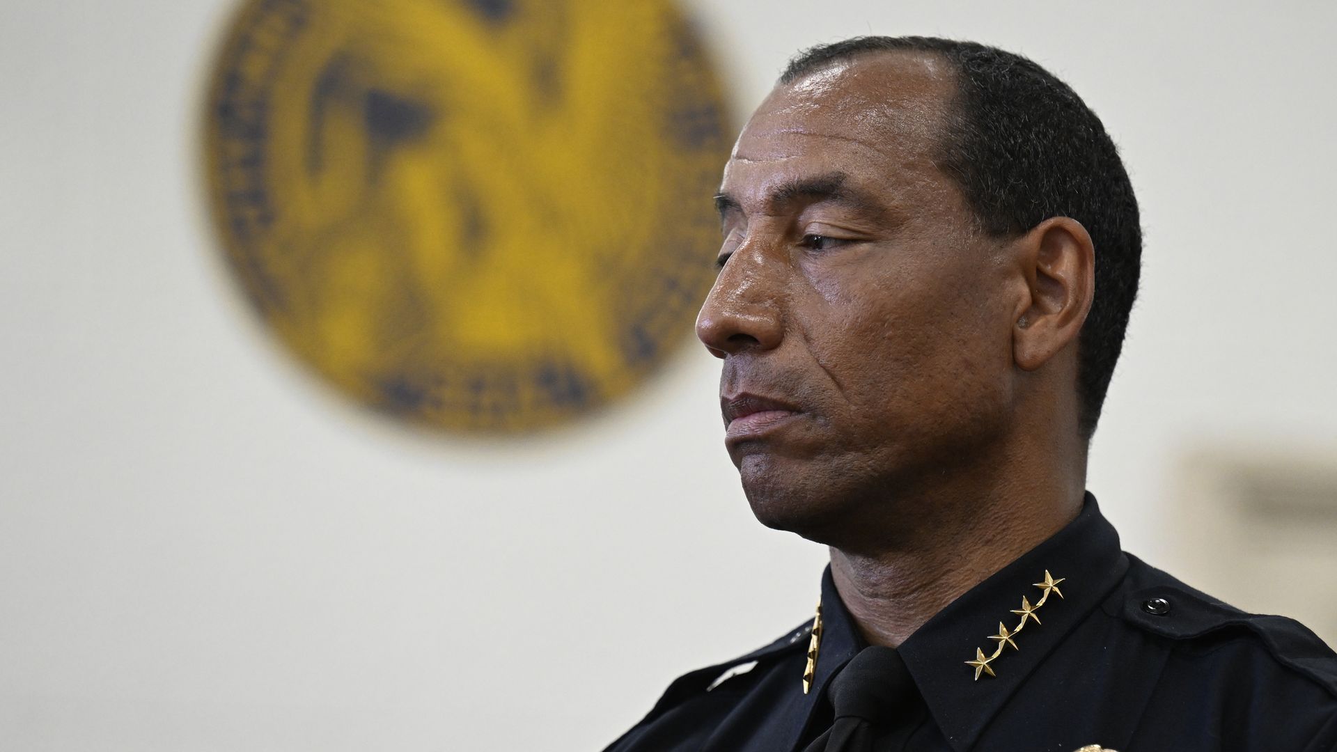 A man in a black police uniform with gold stars stares onwardly. 