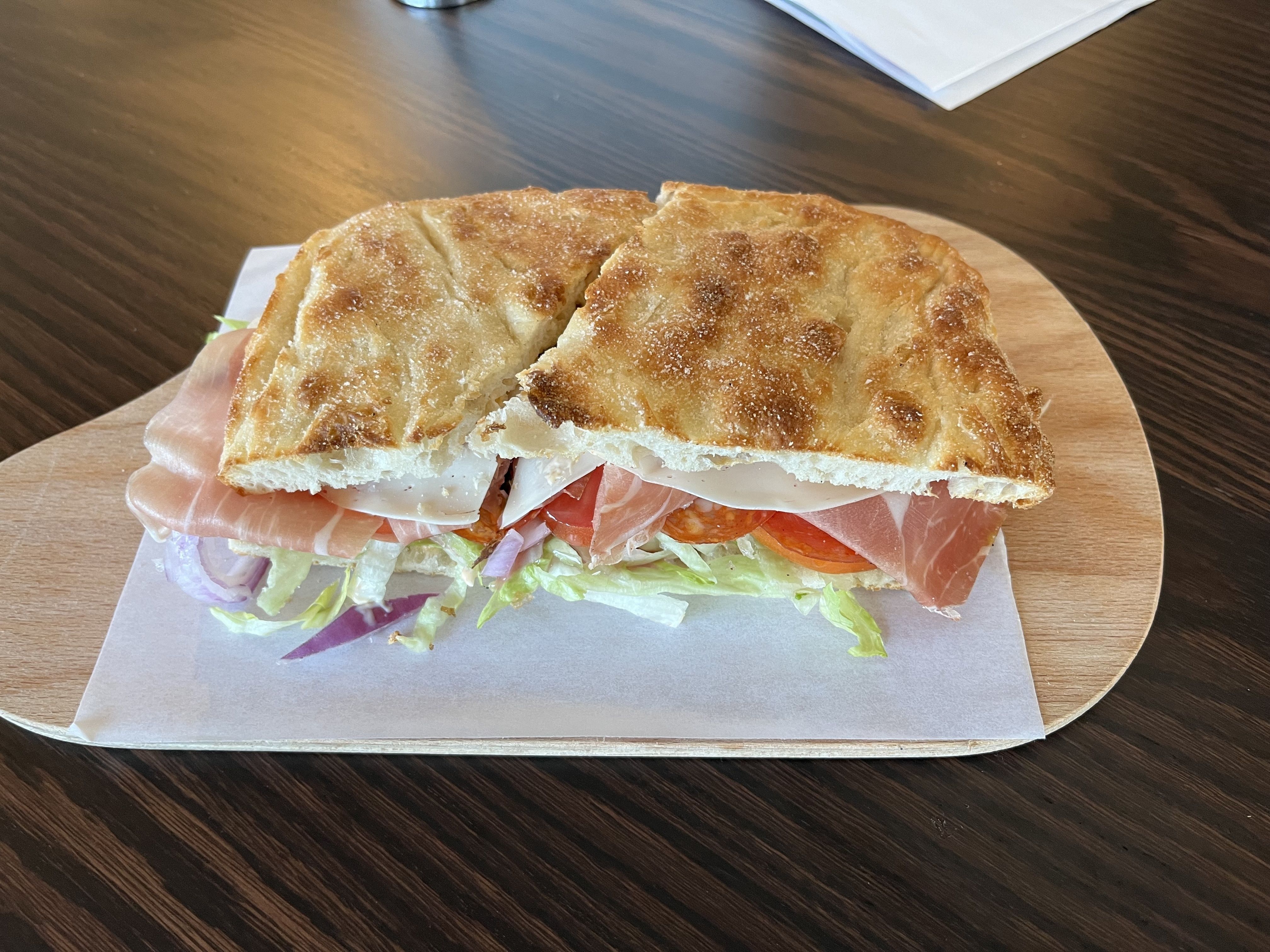 A sandwich filled with cured meats, spicy mayo and giardiniera on bread, on a wooden tray.