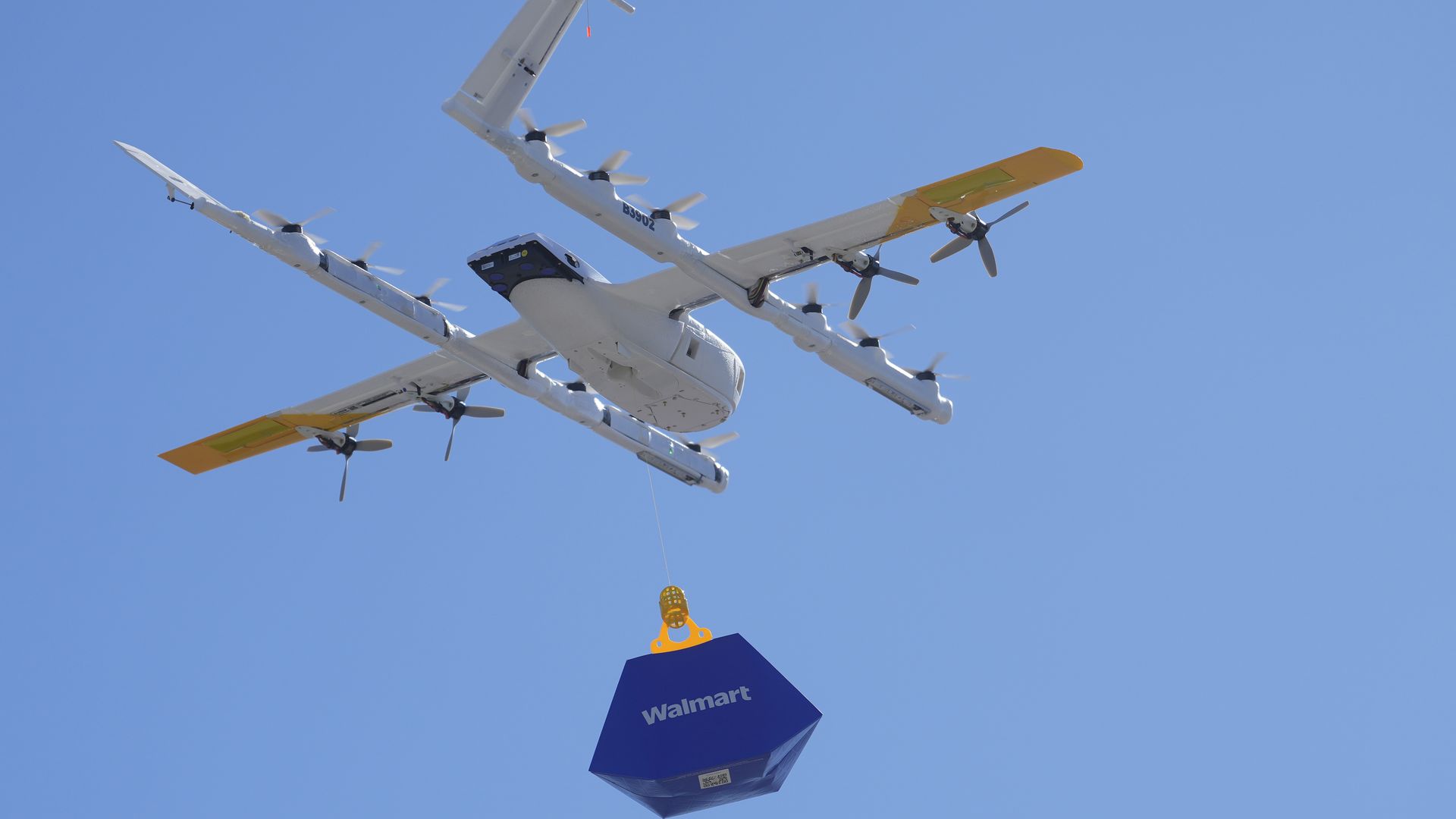 Photo of a drone in the sky carrying a small Walmart box.
