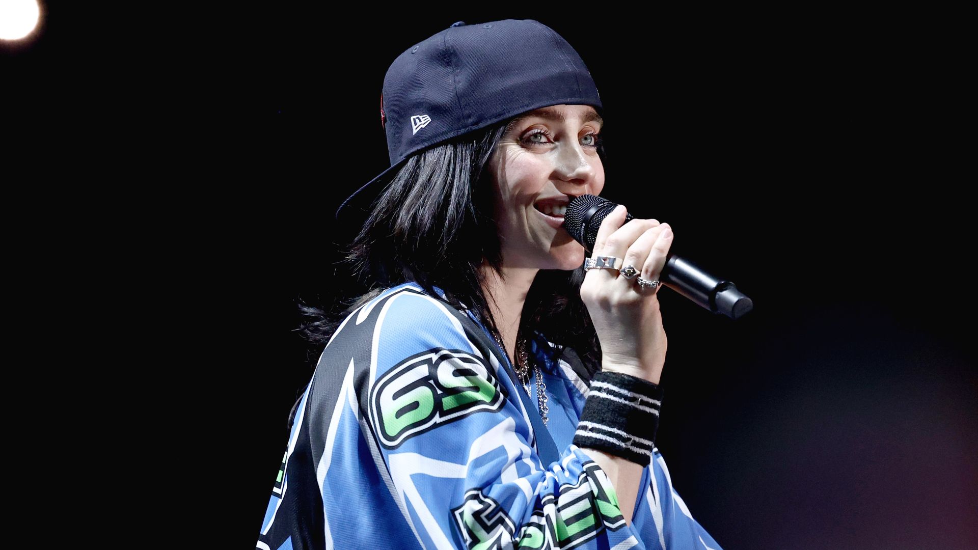 Image shows Billie Eilish with a mic and a hat.
