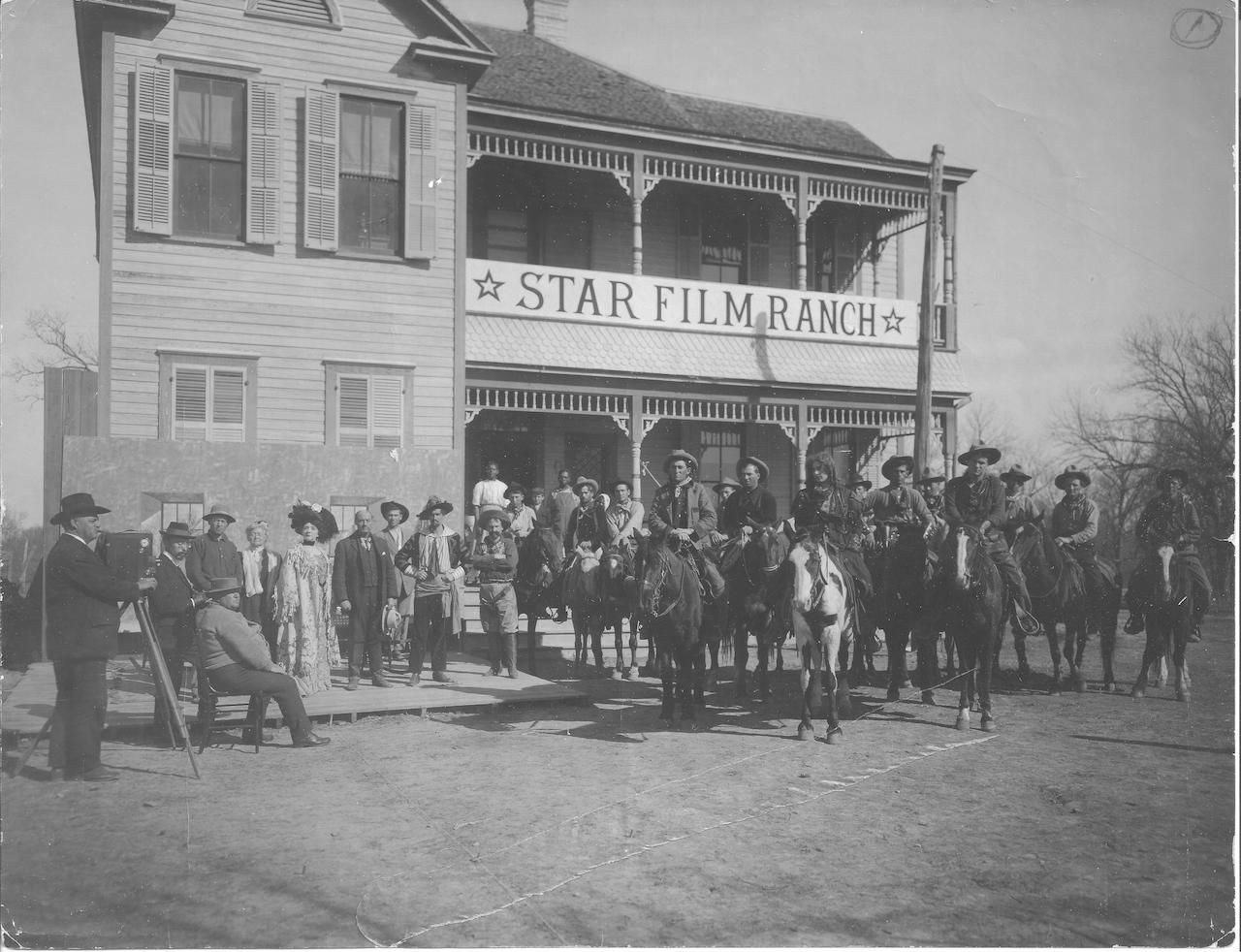 Black-and-white photo of a Western film crew and cast gathered outside a two-story building labeled "Star Film Ranch," with cowboys on horses and onlookers along the street.