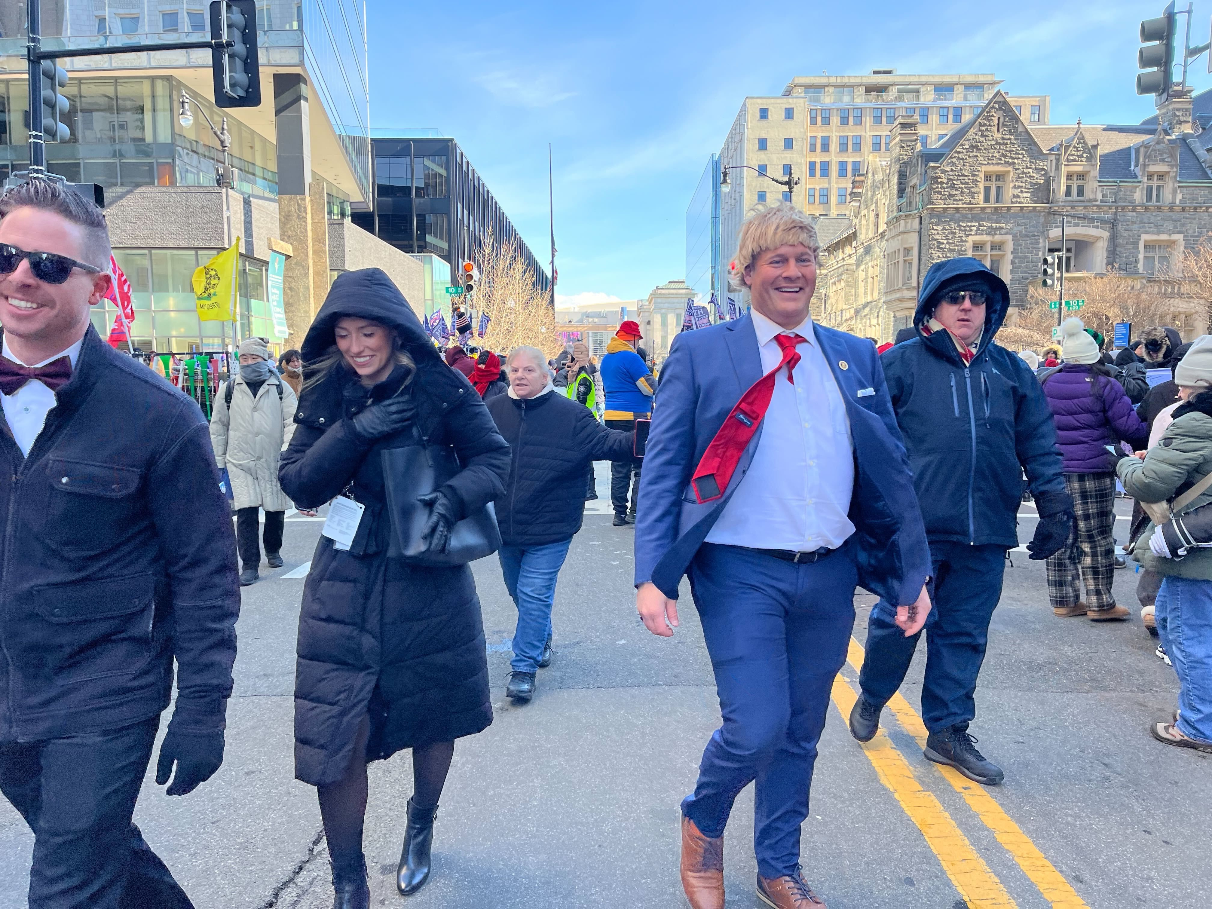 A woman in a black parka and a man in a Donald Trump wig and red tie walking in city streets in DC.