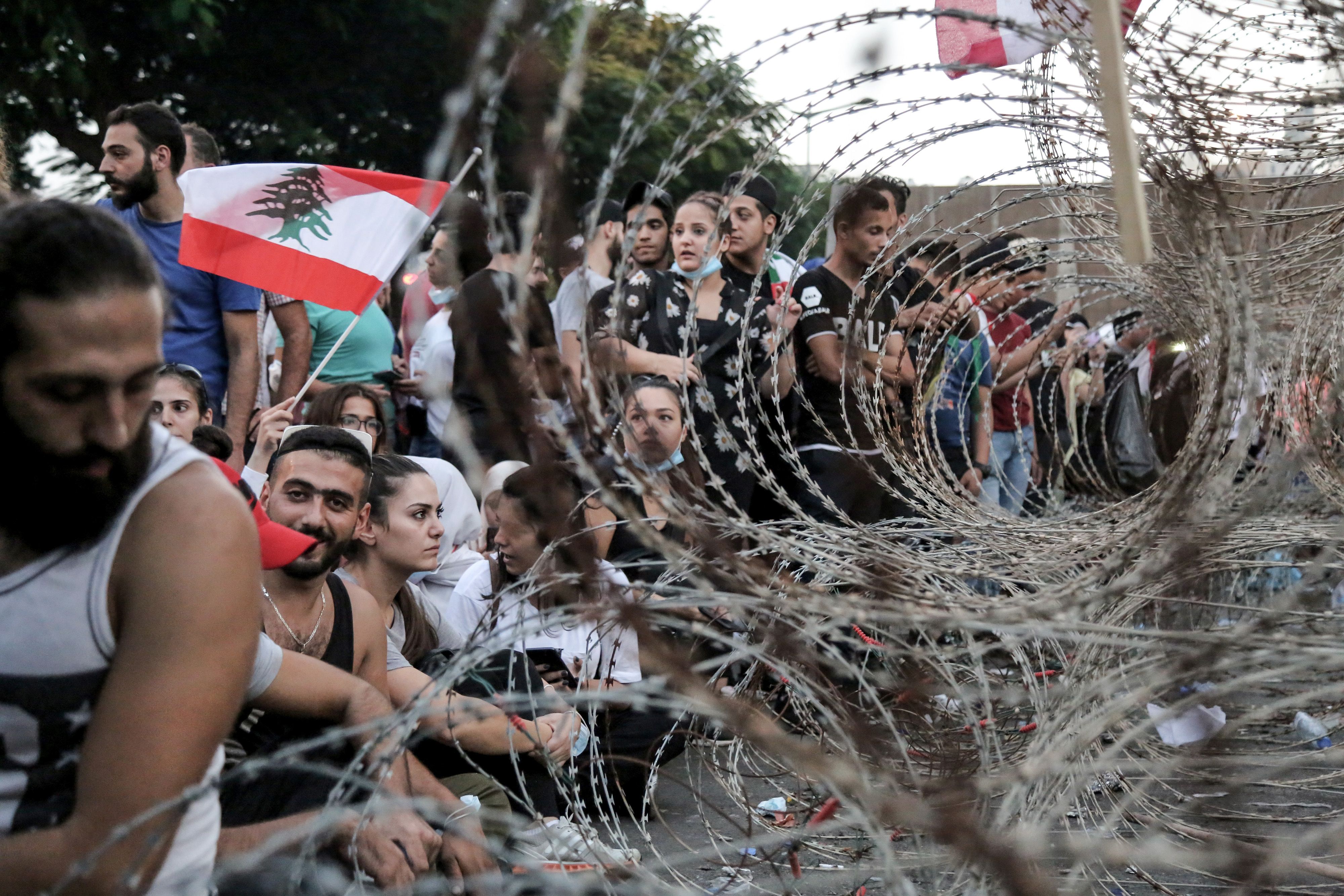 In this image, a line of people waving flags stand behind barbed wire fencing