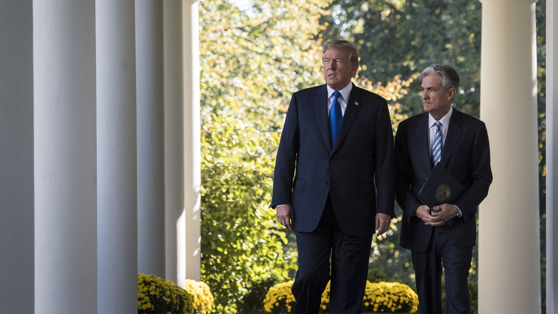 President Trump and Fed Chair Jerome Powell walk side by side under a colonnade at the White House