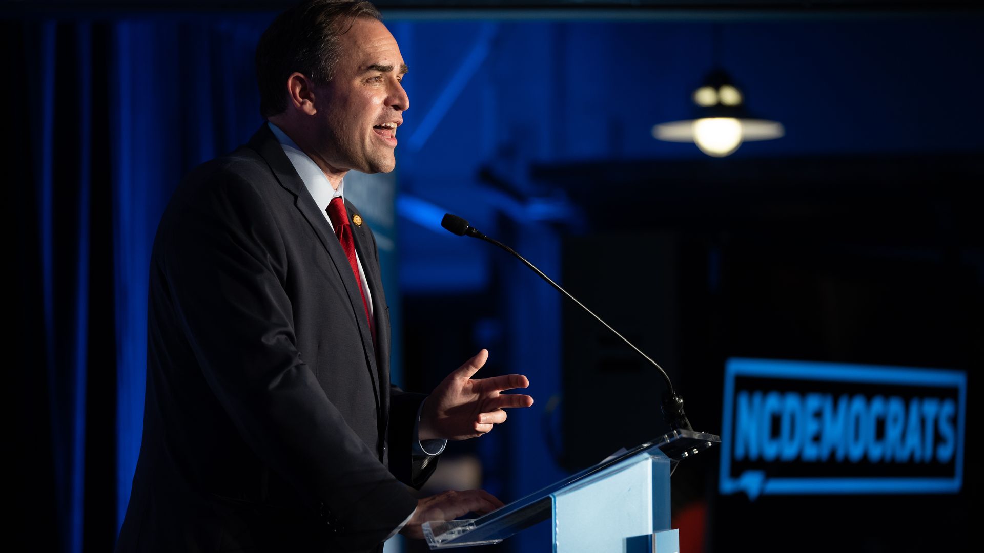 Wiley Nickel speaking behind a lectern with an NC Democrats logo behind him