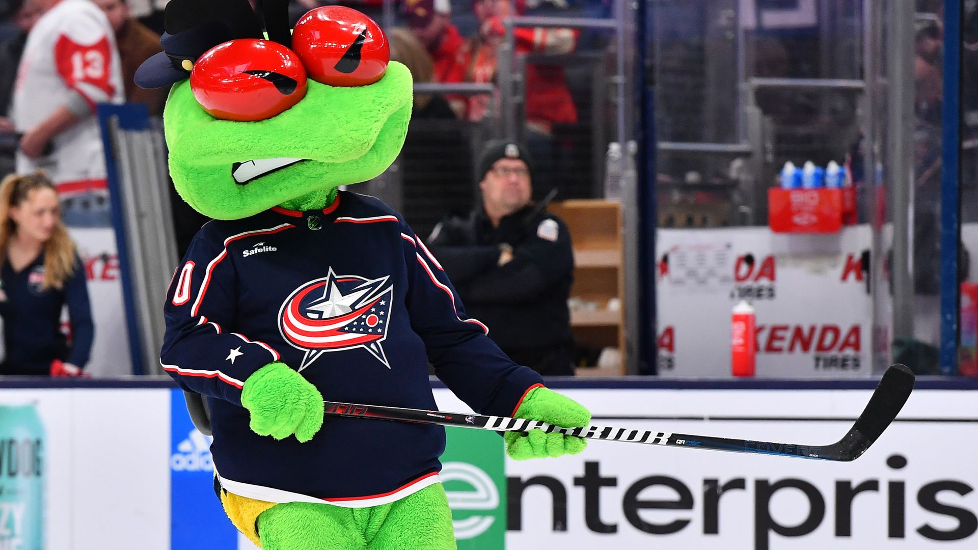Blue Jackets mascot Stinger skates on the ice holding a hockey stick. 