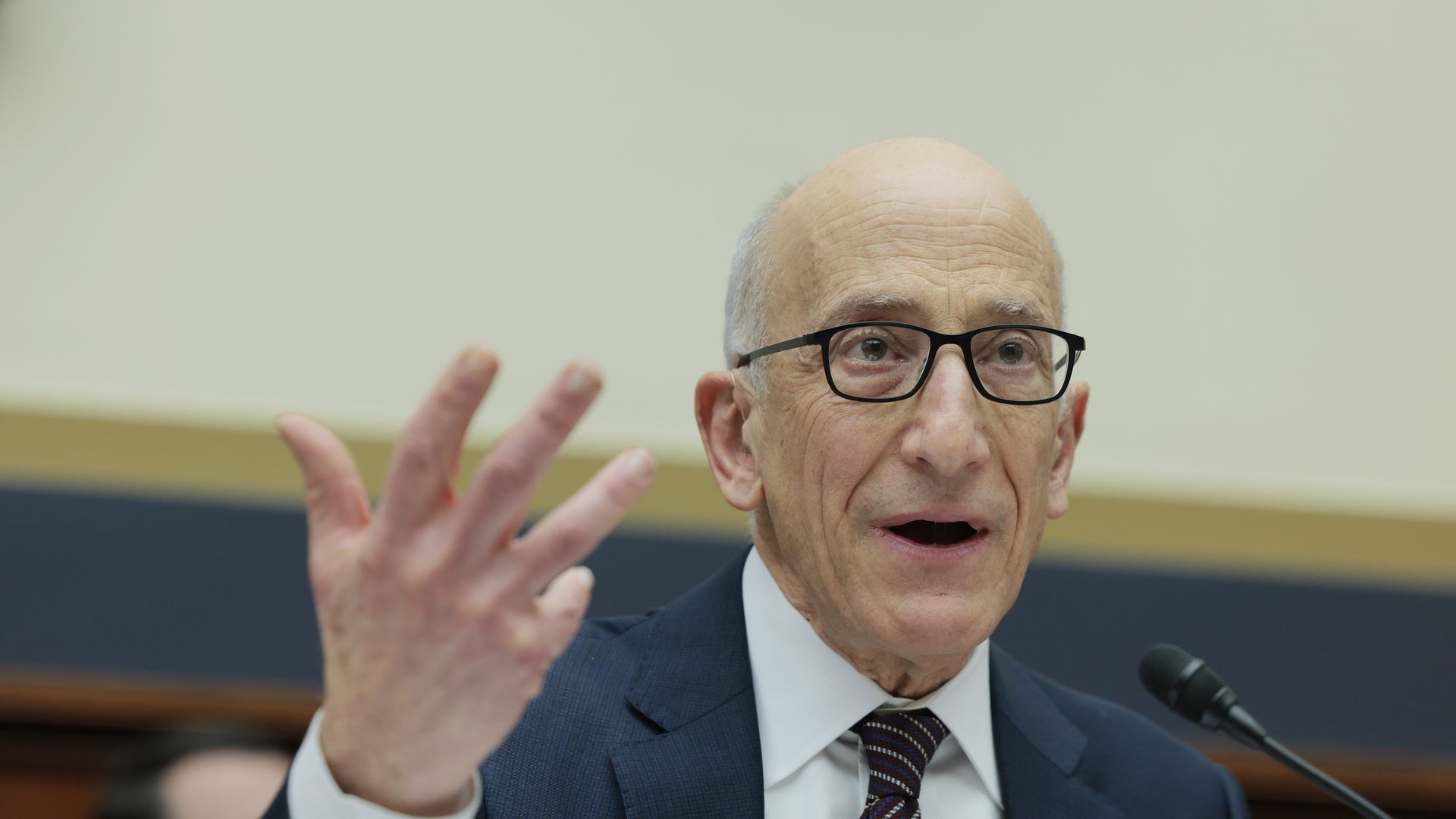 An older man speaking on a microphone while seated.