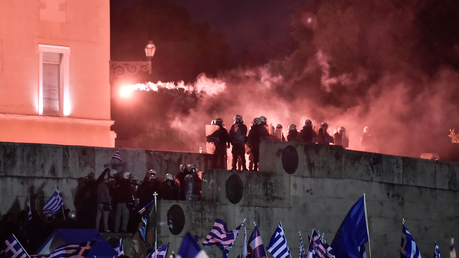 Protesters with Greek flags throw flares near riot police outside Greek Parliament.