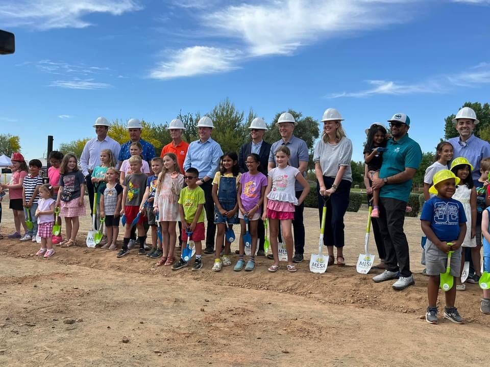 Kids and adults in hard hats with shovels. 