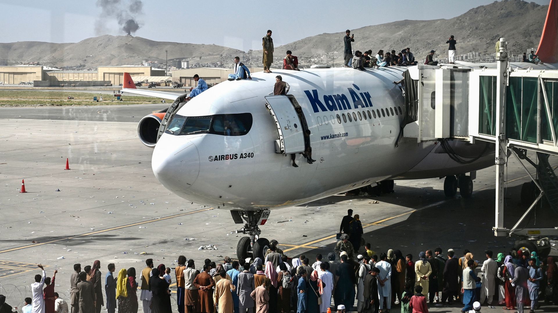 Afghan people climb atop a plane as they wait at the Kabul airport in Kabul on August 16, 2021
