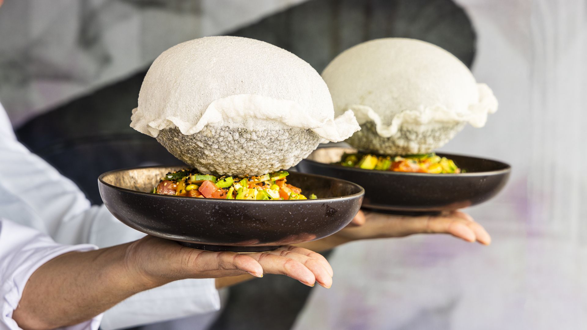 "Clouds" of rice paper with poke in black bowls being carried by servers 