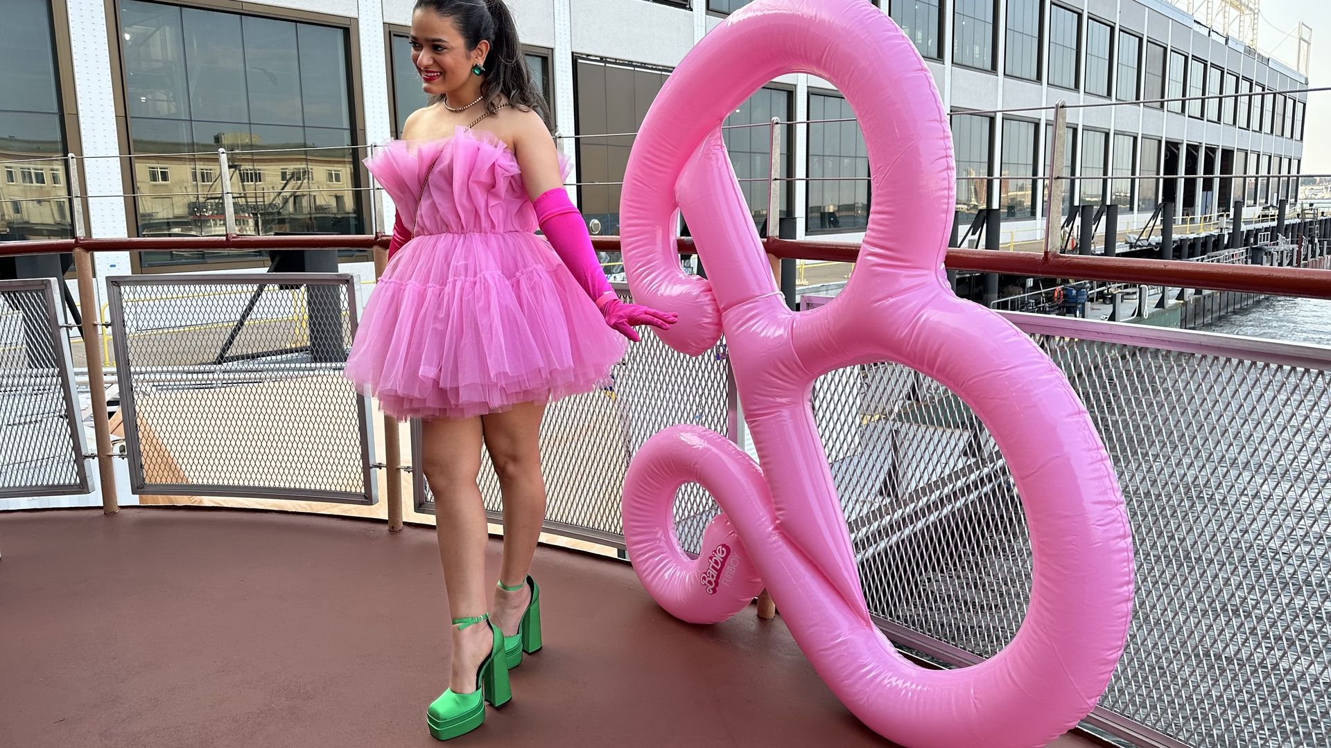 Mallika Singh, wearing a puffy pink dress and emerald green heels, poses for a photo with an inflatable B on the Barbie boat cruise in the Seaport.