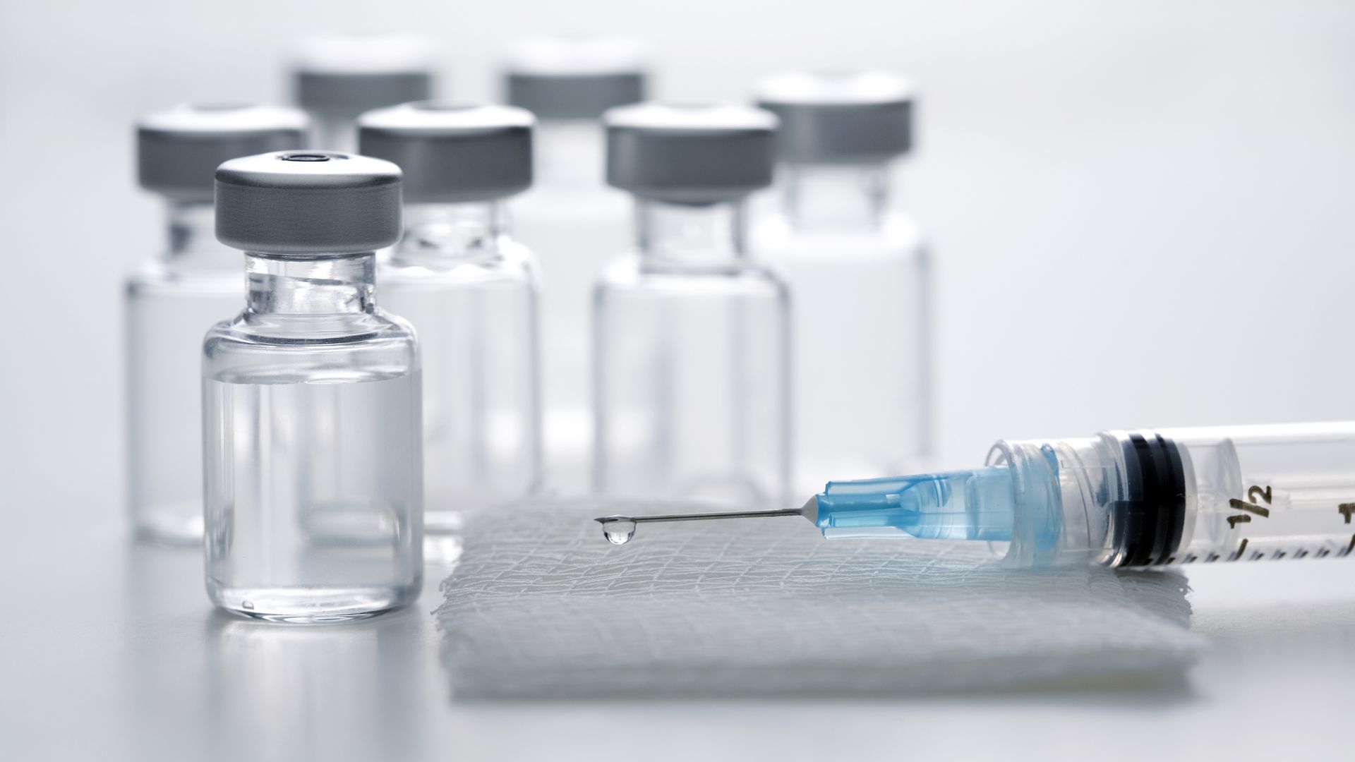 Syringe on gauze pad surrounded by vaccine bottles
