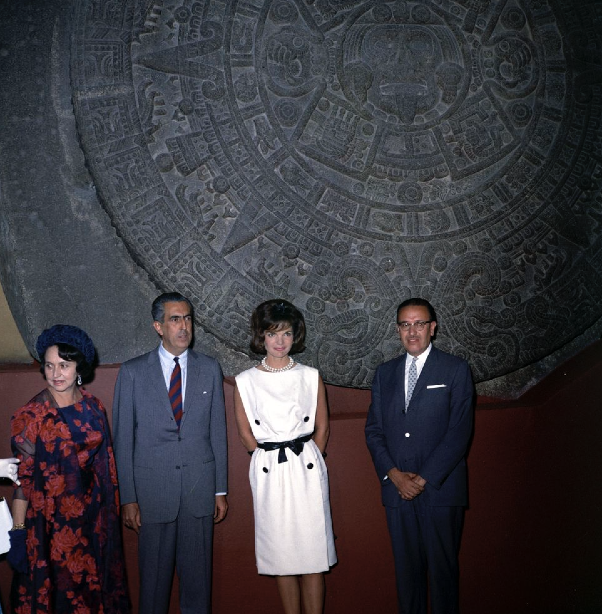 First Lady Jacqueline Kennedy poses in front of the Piedra del Sol (Aztec calendar, Sun Stone) during a tour of the Museo Nacional de Antropología (National Museum of Anthropology) of the Instituto Nacional de Antropología e Historia (National Institute of Anthropology and History) in Mexico City.