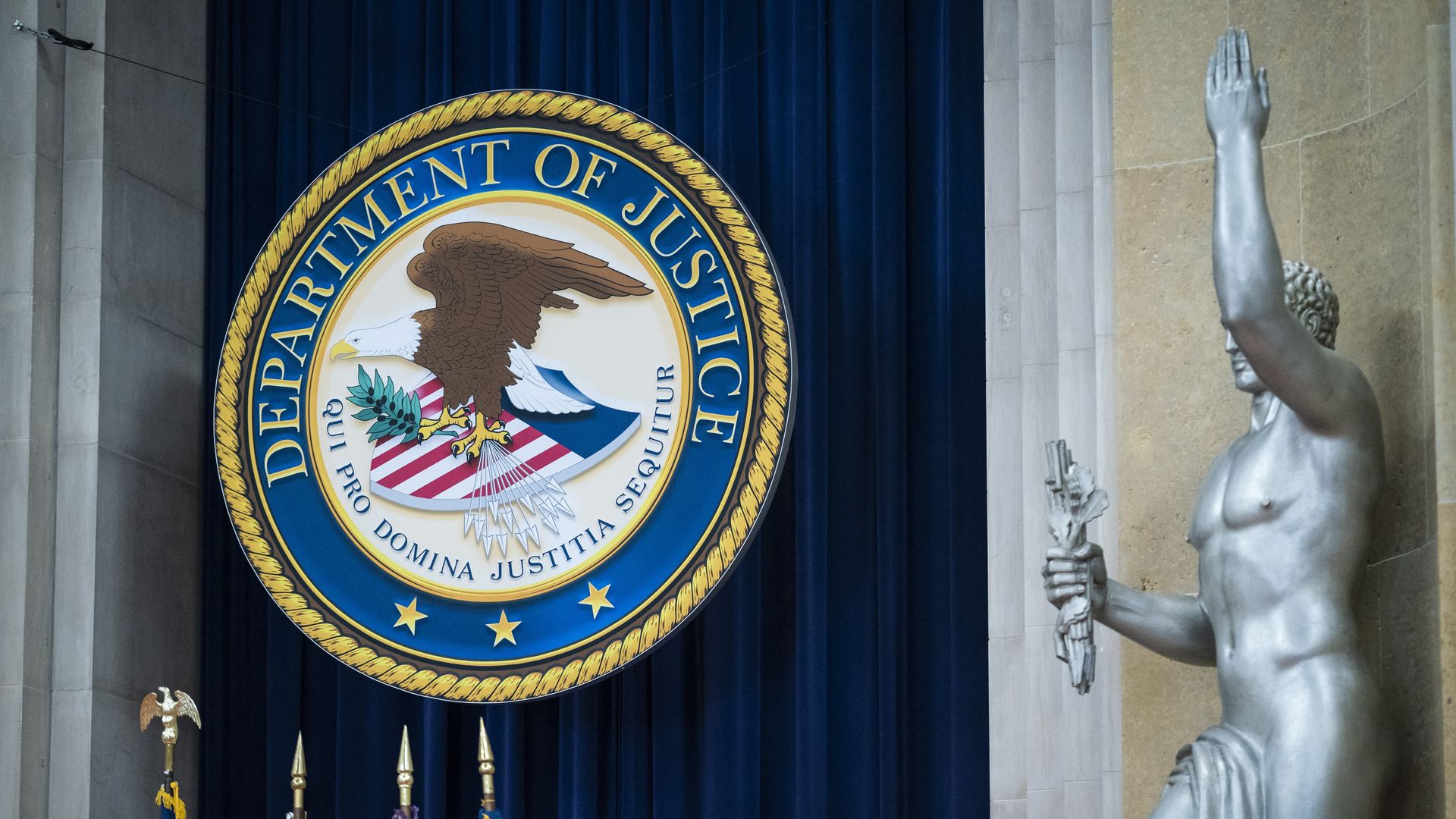 Department of Justice seal next to a statue of a man with his arm raised.