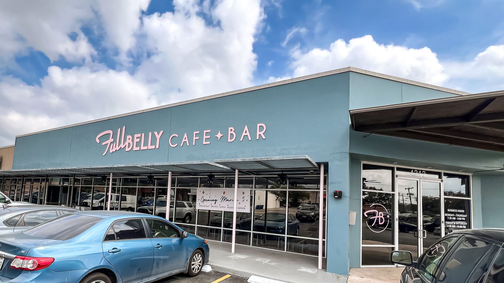 A teal building with a retro-style sign for "Full Belly Cafe + Bar" with a blue sky behind it.