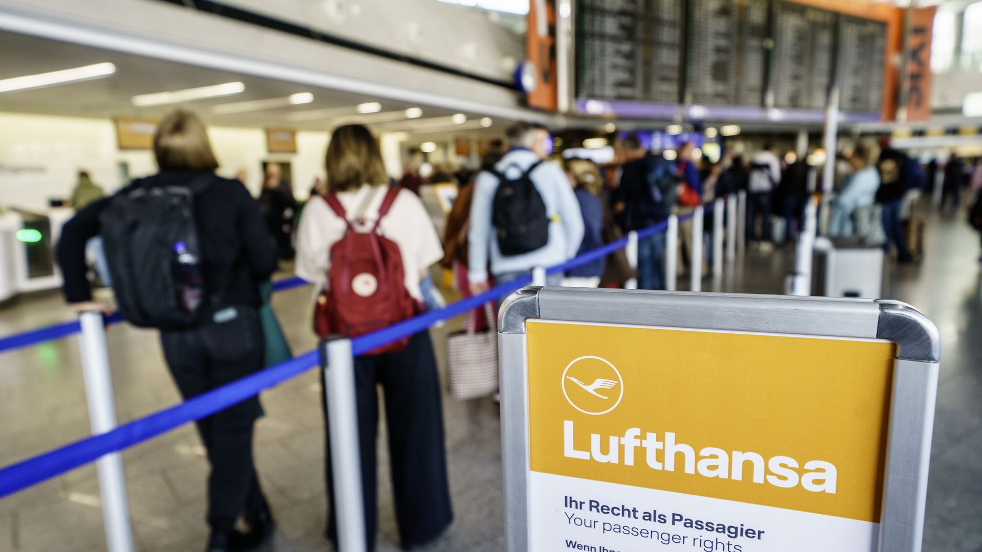 A sign for Lufthansa passenger rights sits by a line of passengers in an airport in Germany.