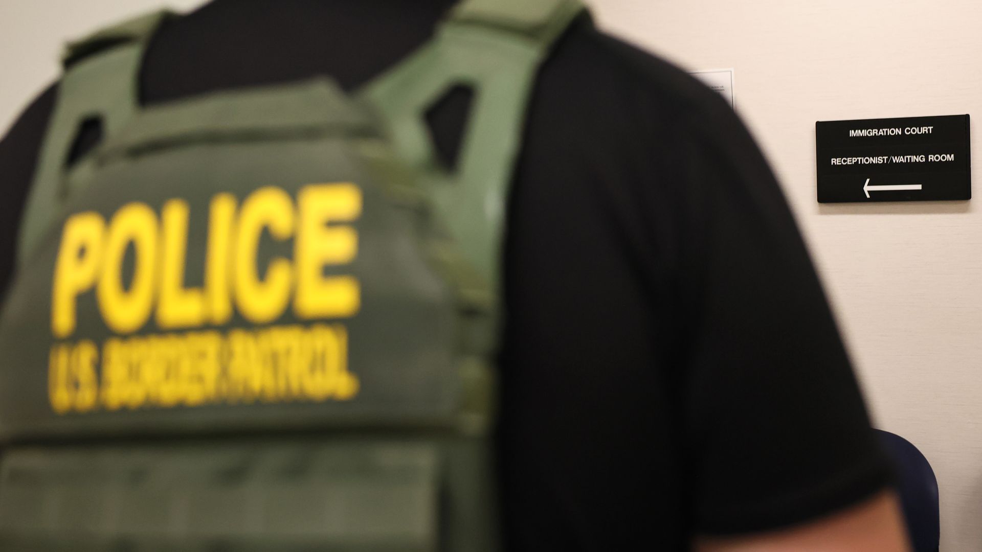 Photo of an ICE officer's back as they wait in front of a sign that points to immigration court