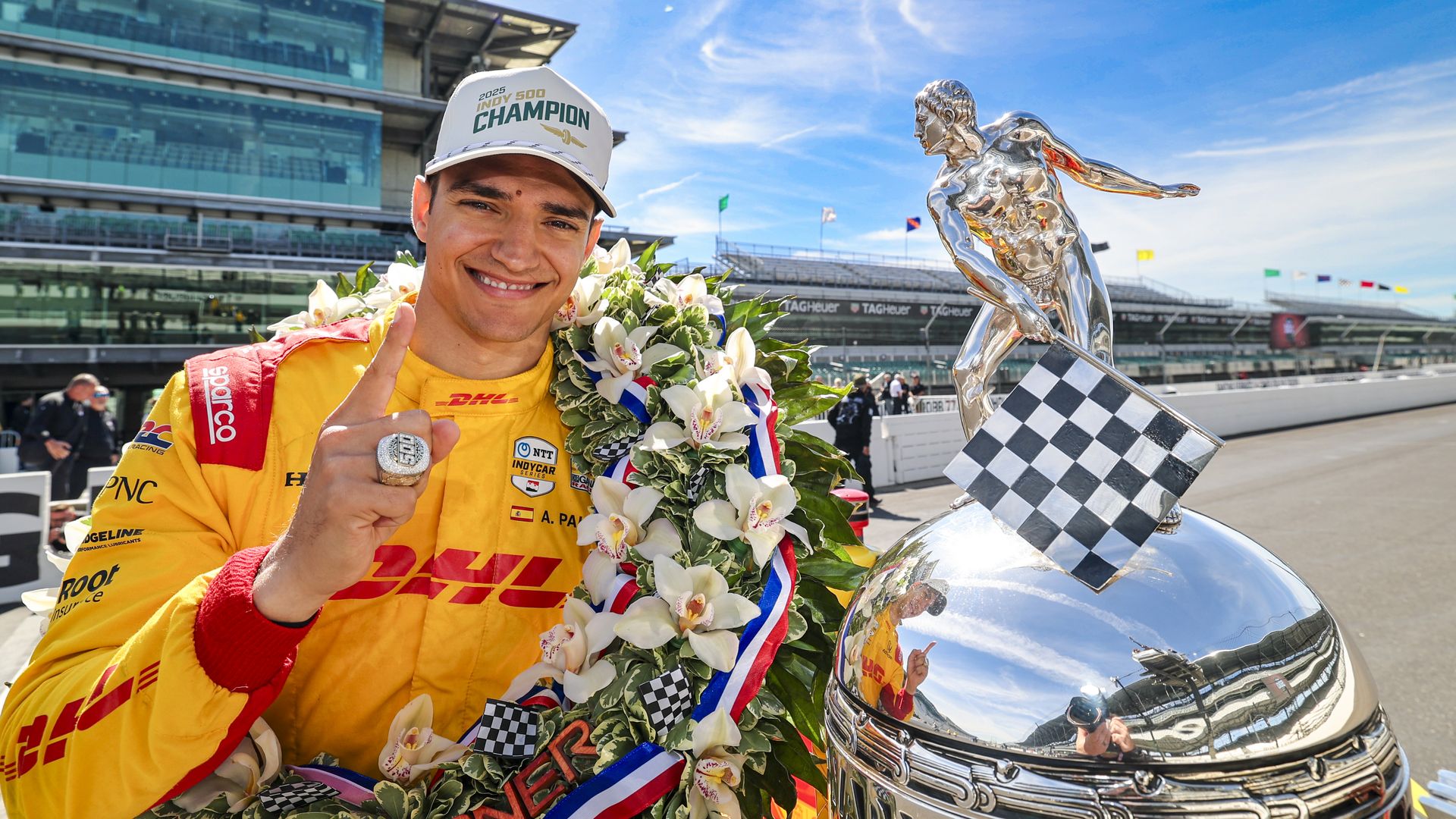 A man in a racing suit next to a trophy.