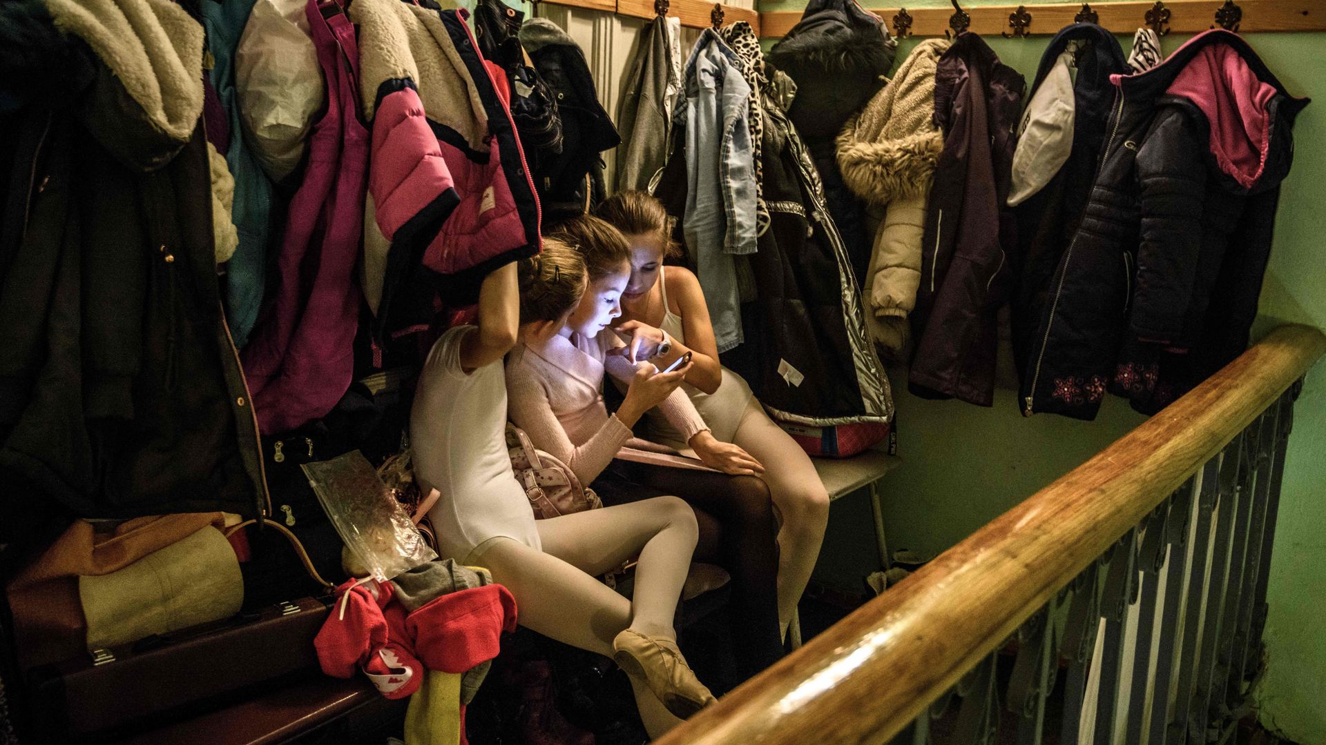 Young girls use a smartphone in a coat room.
