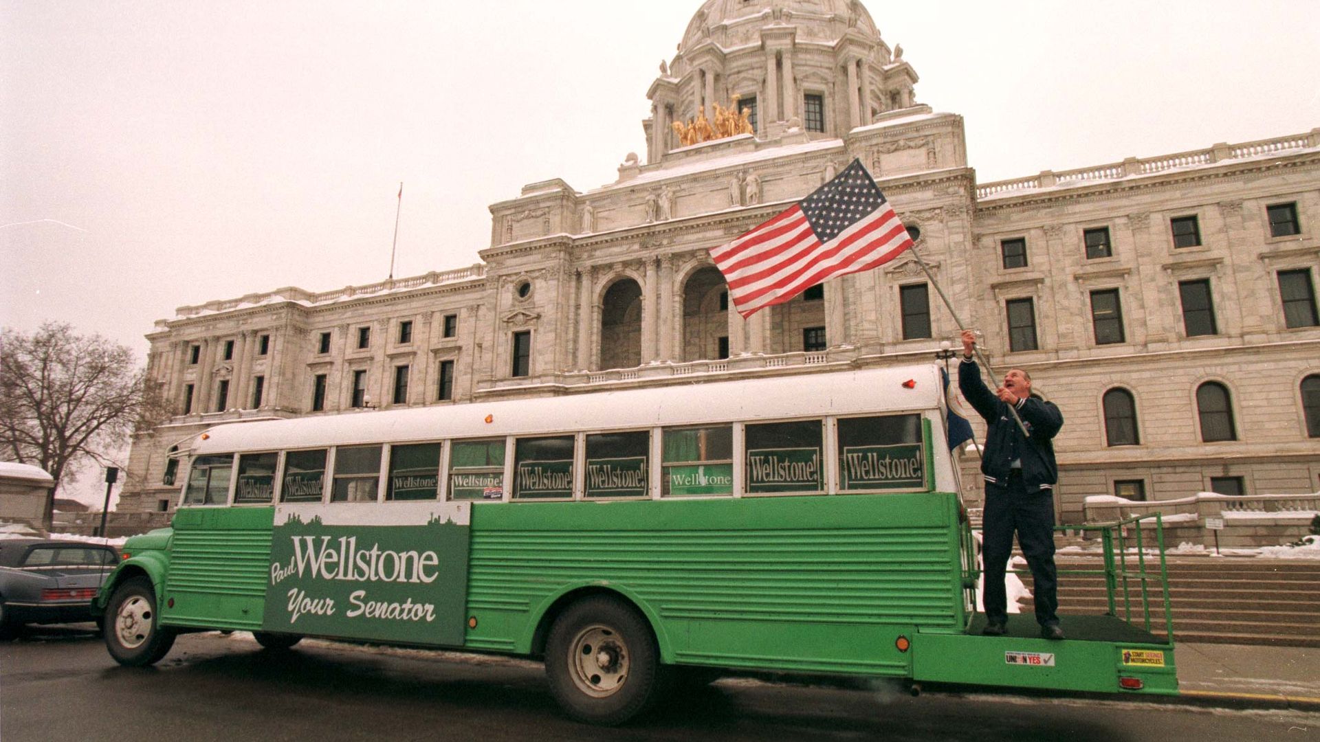 A photo of a green school bus with a sign on the side reading "Wellstone: Your Senator"