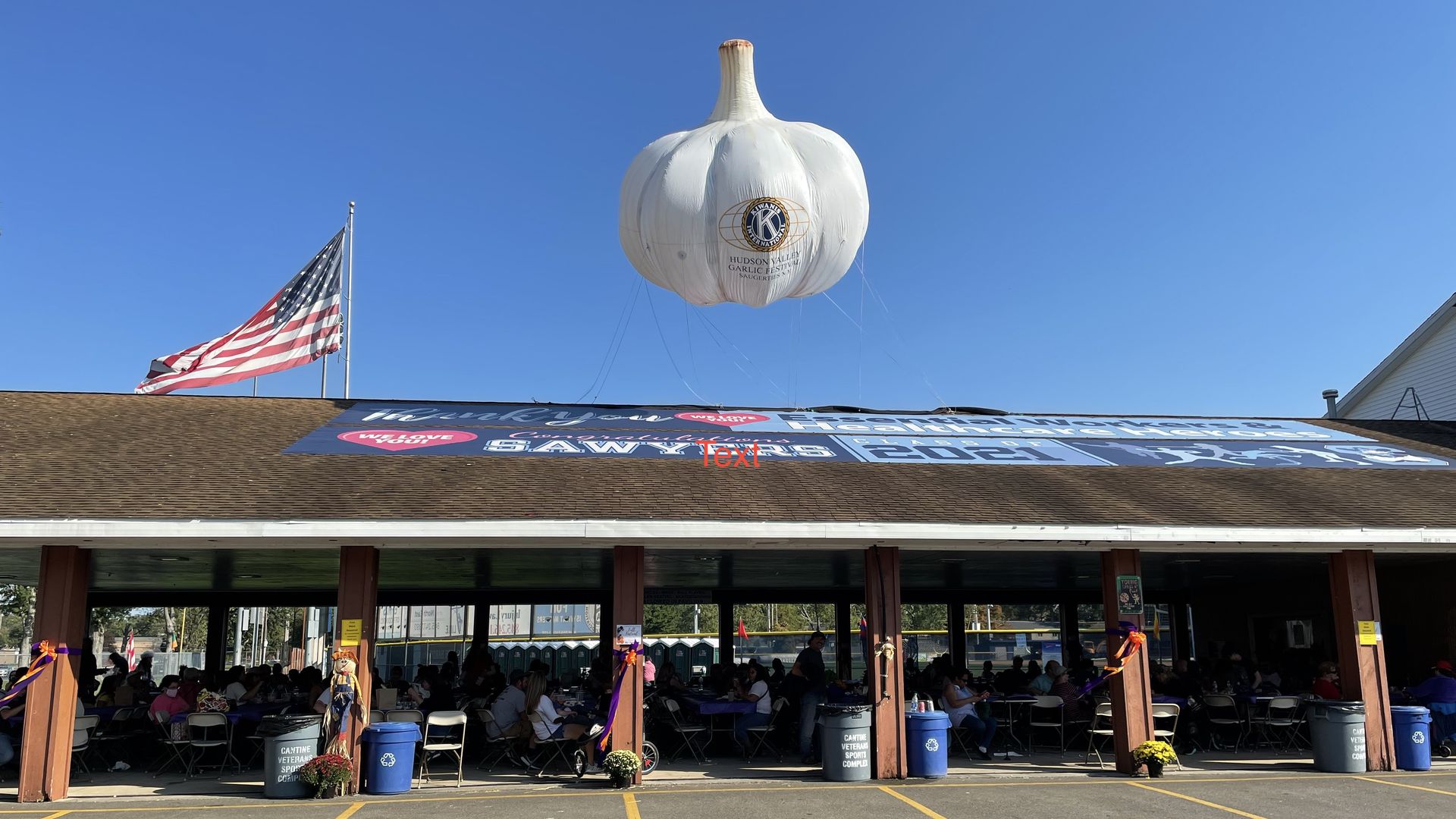 A large inflatable garlic bulb flying over a shed-style building alongside an American flag.