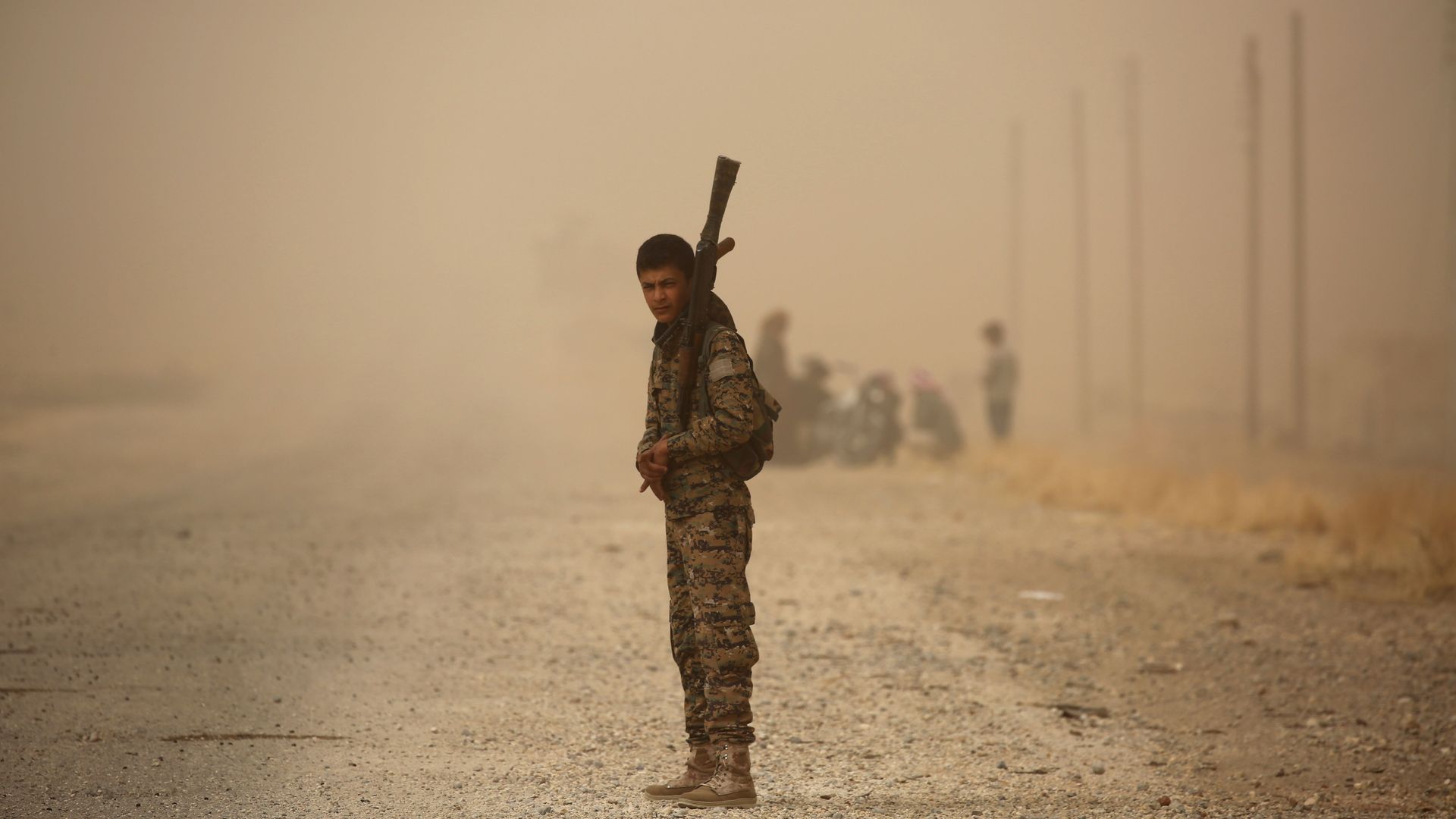 A member of the Syrian Democratic Forces stands with a weapon in a sandstorm.