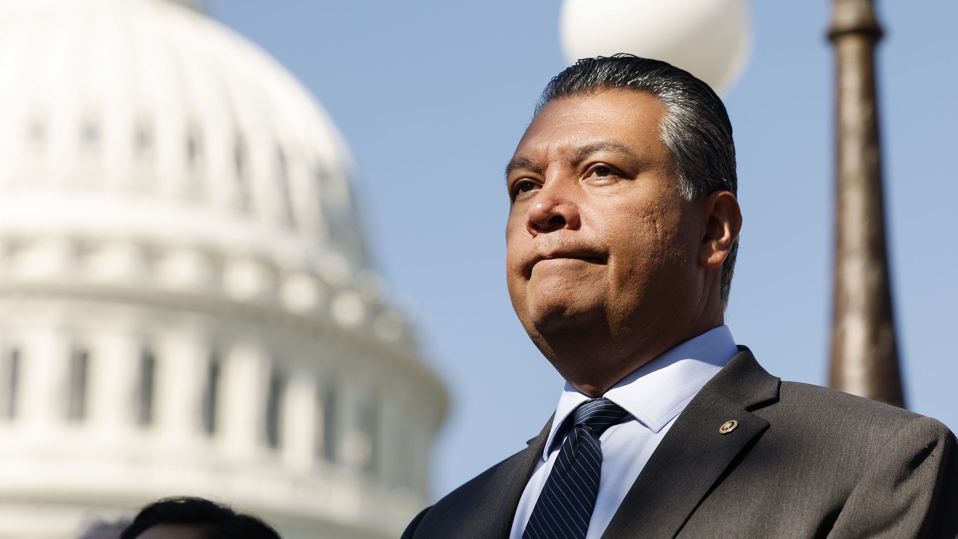 California Senator Alex Padilla stands in front of the U.S. Capitol with a blue sky behind him