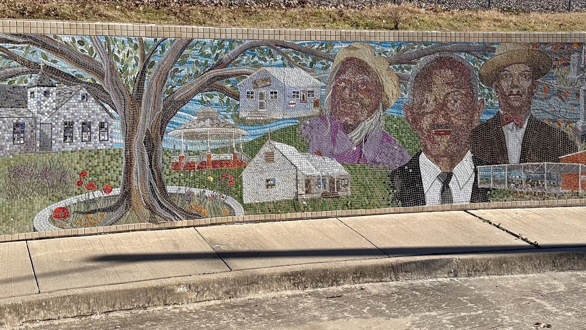 A photo of a tile mural of a neighborhood, a tree and three faces